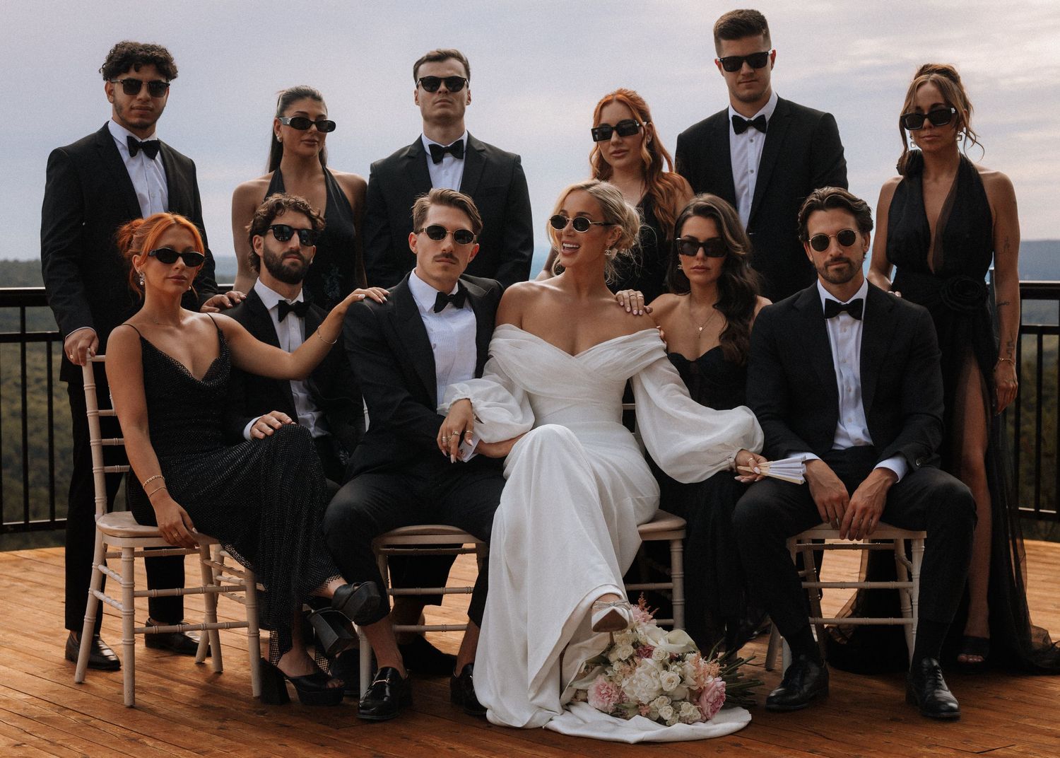 Wedding party in formal attire and sunglasses posing outdoors.