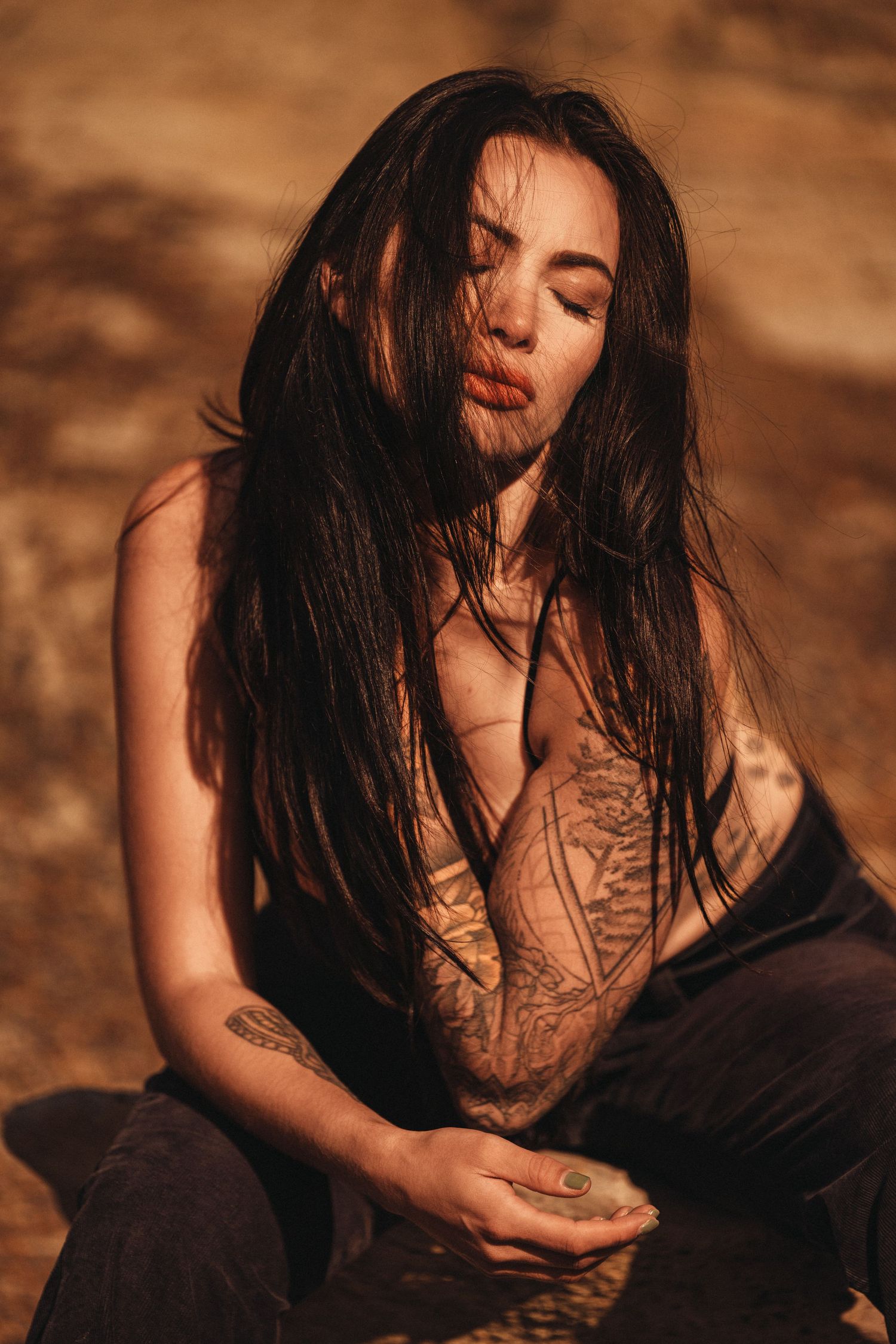 Artistic portrait with warm tones featuring long dark hair and visible tattoos.