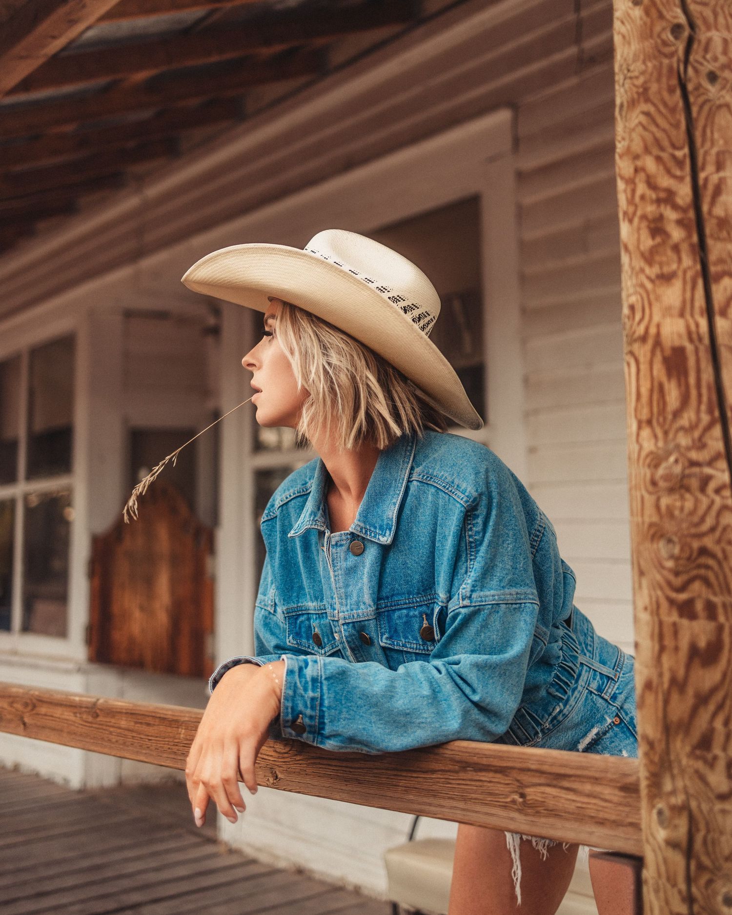 Person in denim rests on wooden porch railing at rustic building.