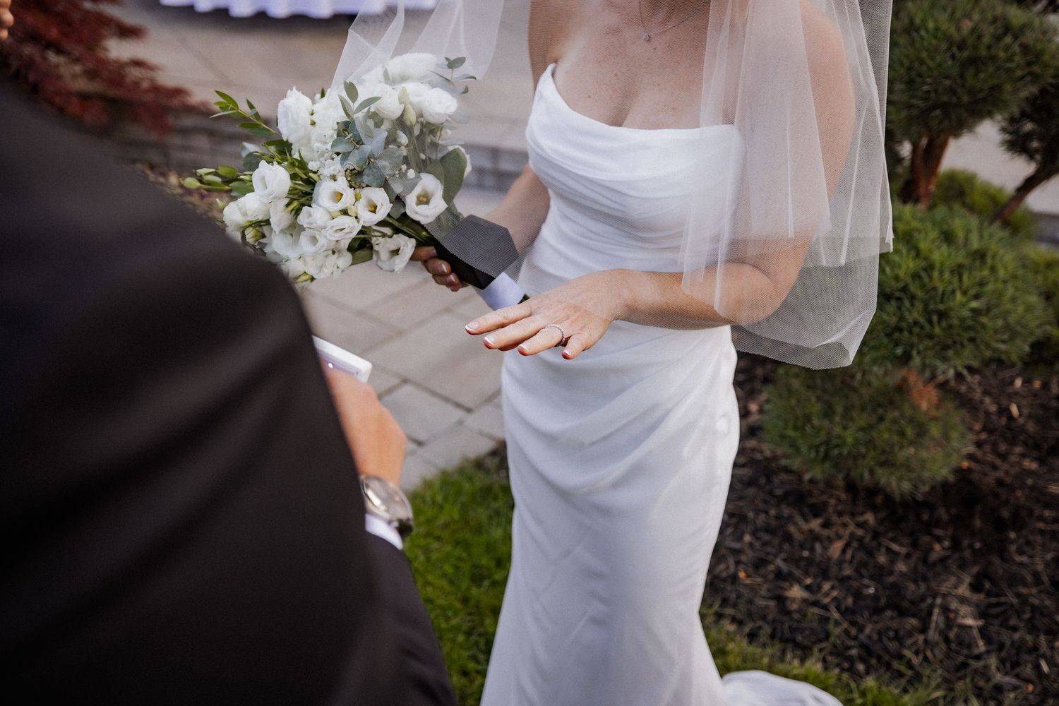 Wedding ceremony details showing white dress and veil against garden backdrop.