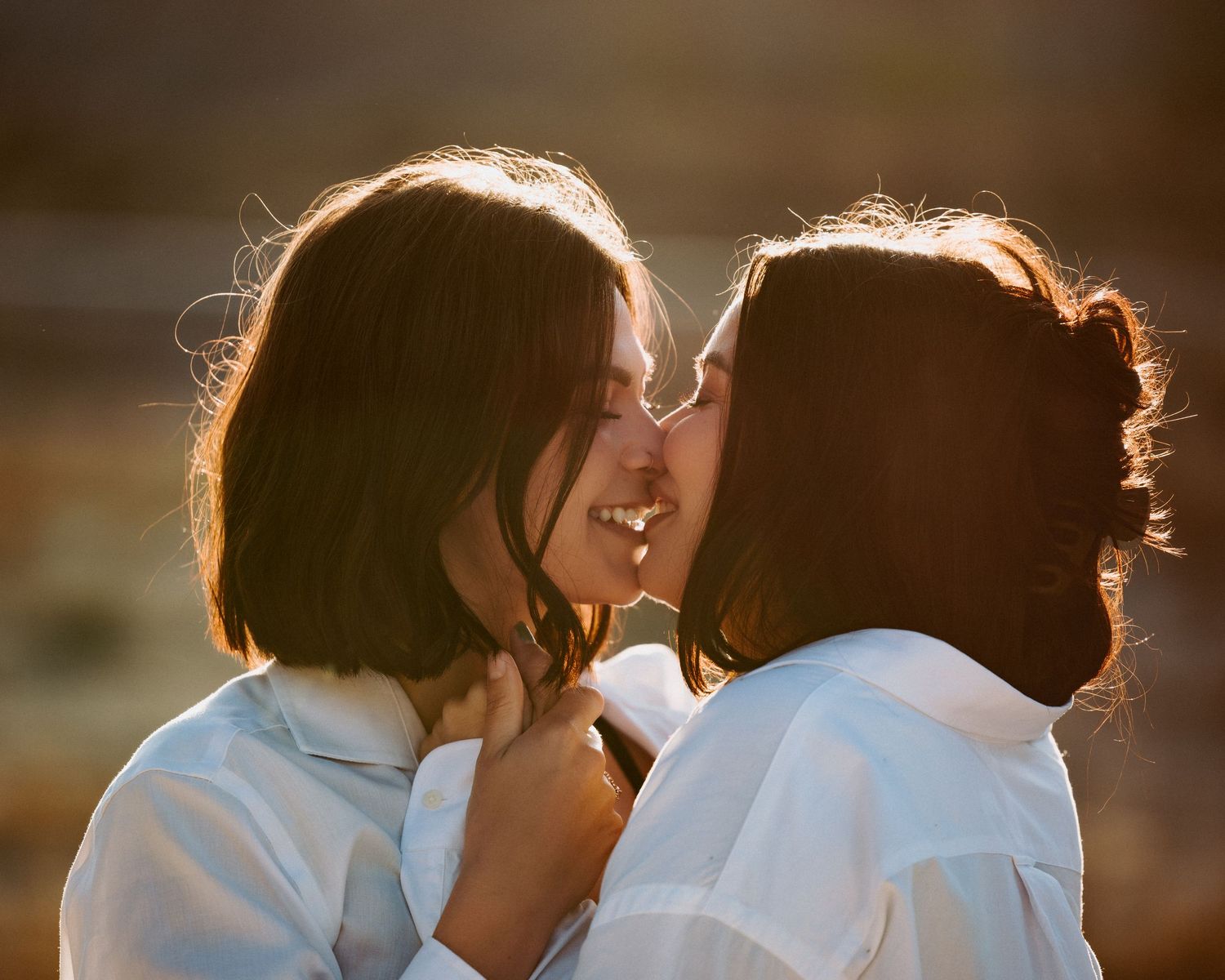 Silhouetted figures in white clothing share intimate moment at golden hour.