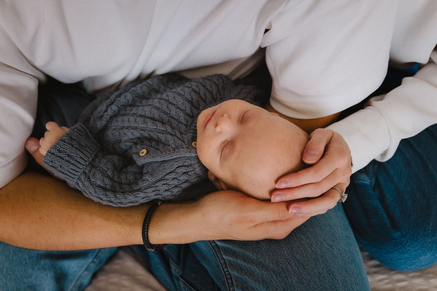 Close-up of hands cradling a sleeping baby wearing a gray knit sweater.