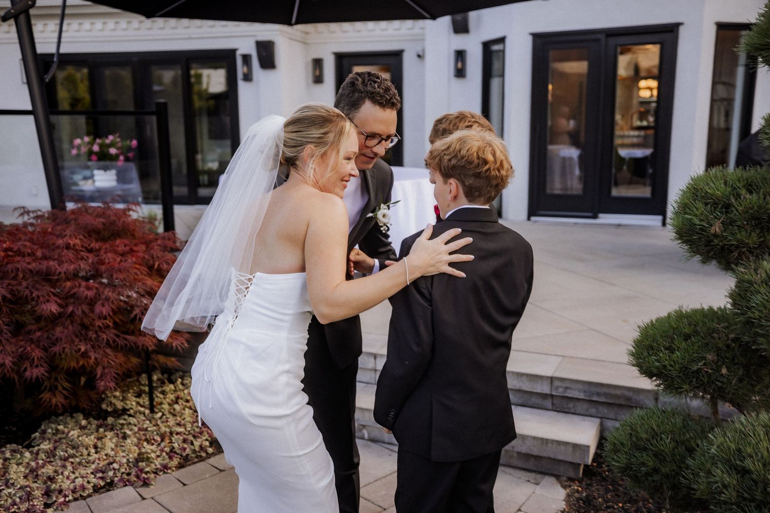 Wedding party sharing an emotional moment outside a modern venue with red landscaping.