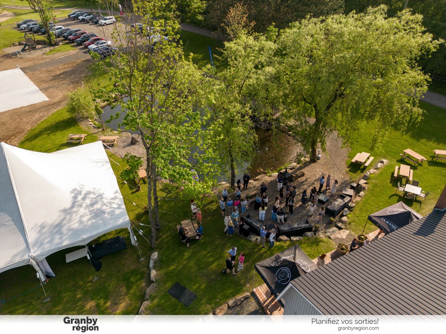 Aerial view of an outdoor event space with tents and gathering areas surrounded by green landscape.