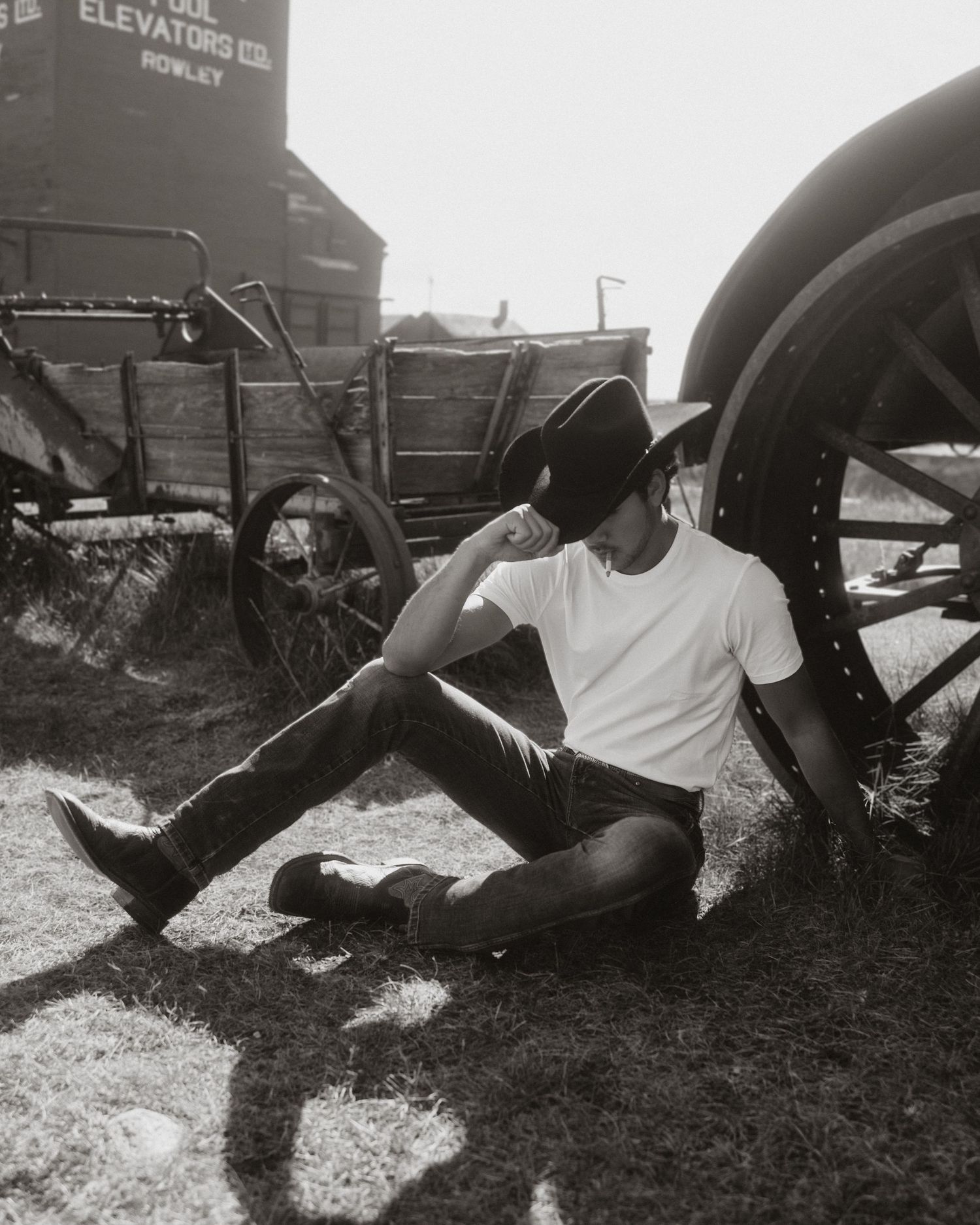 Person in white shirt relaxing by vintage train car in black and white photo.