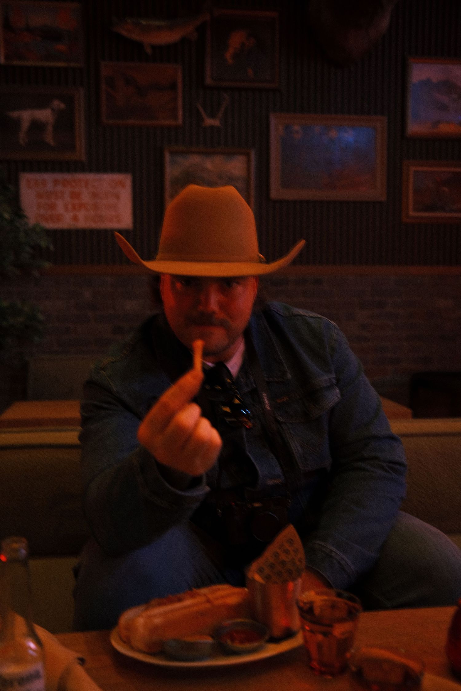 Man in cowboy hat eating at a dimly lit restaurant booth with framed western artwork on the walls.