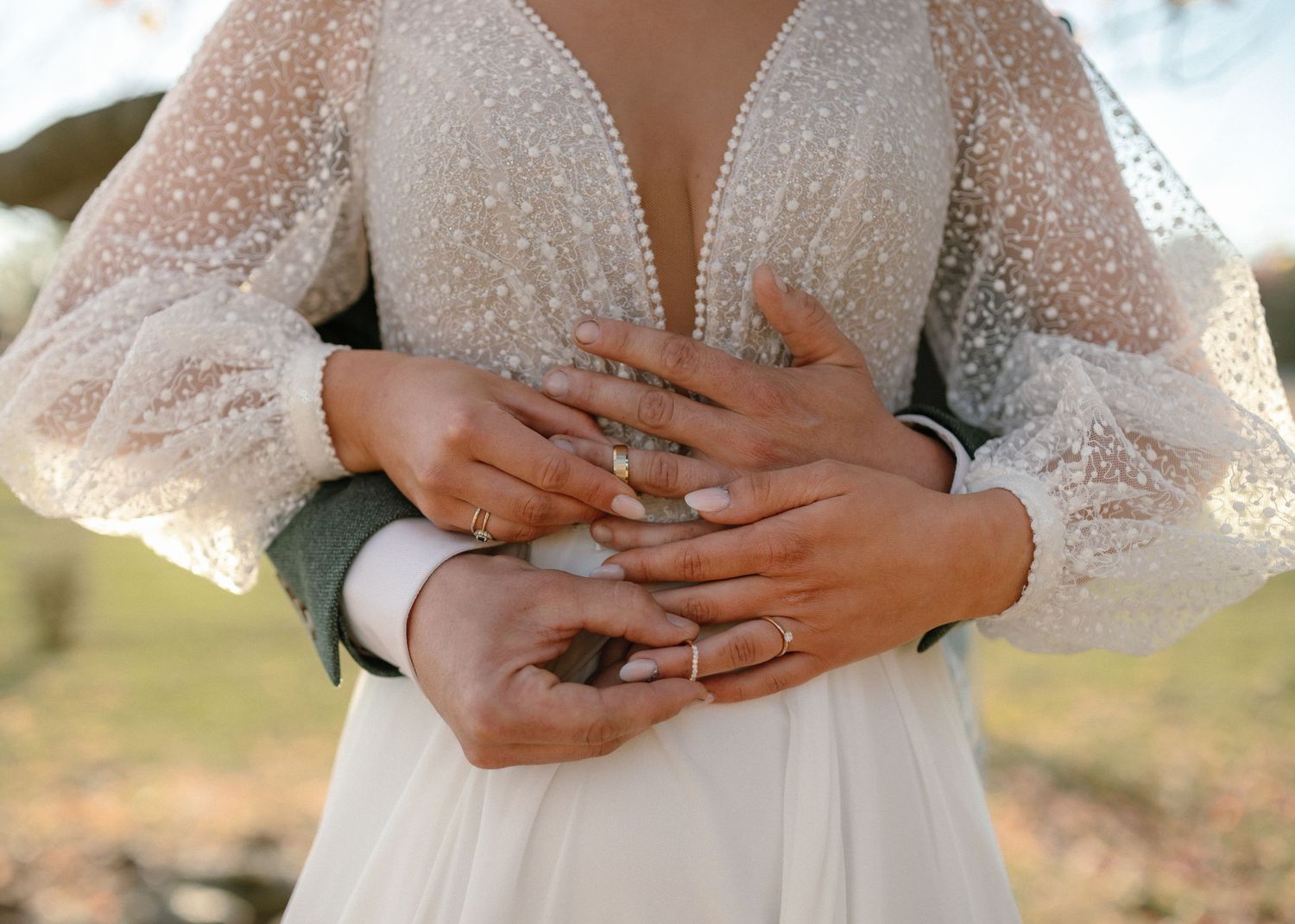 Detail shot of hands with wedding rings against a sparkly white wedding dress bodice.