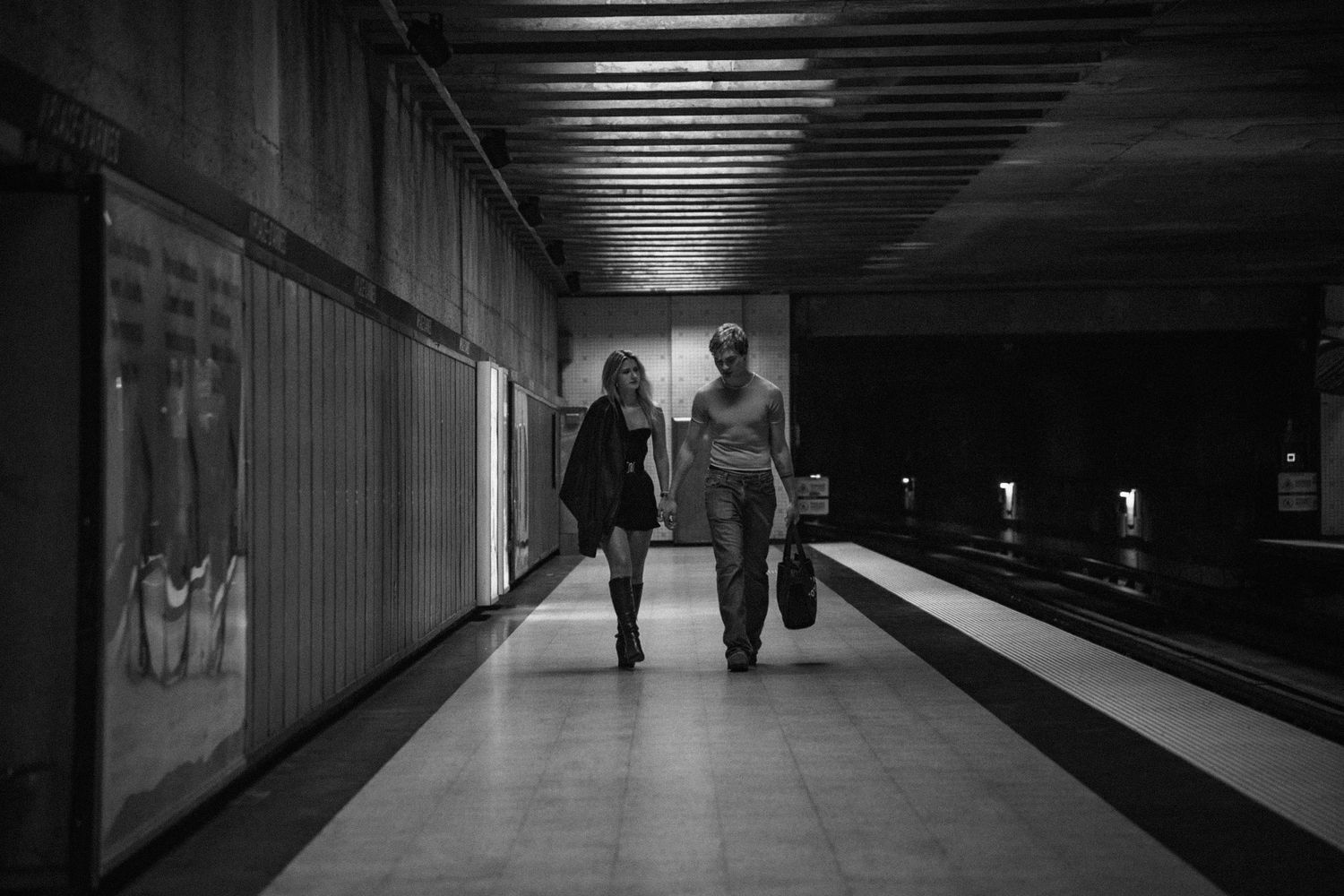 Couple walking together in a dimly lit subway station corridor.