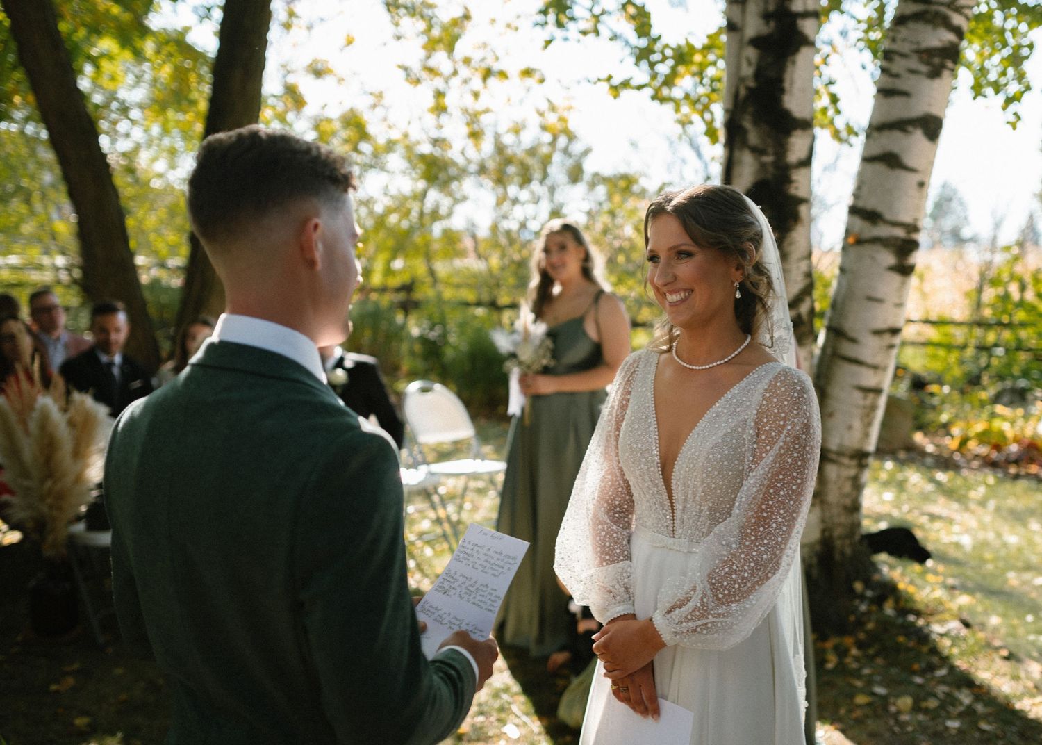Wedding couple exchanging vows in a sunlit outdoor ceremony surrounded by birch trees.