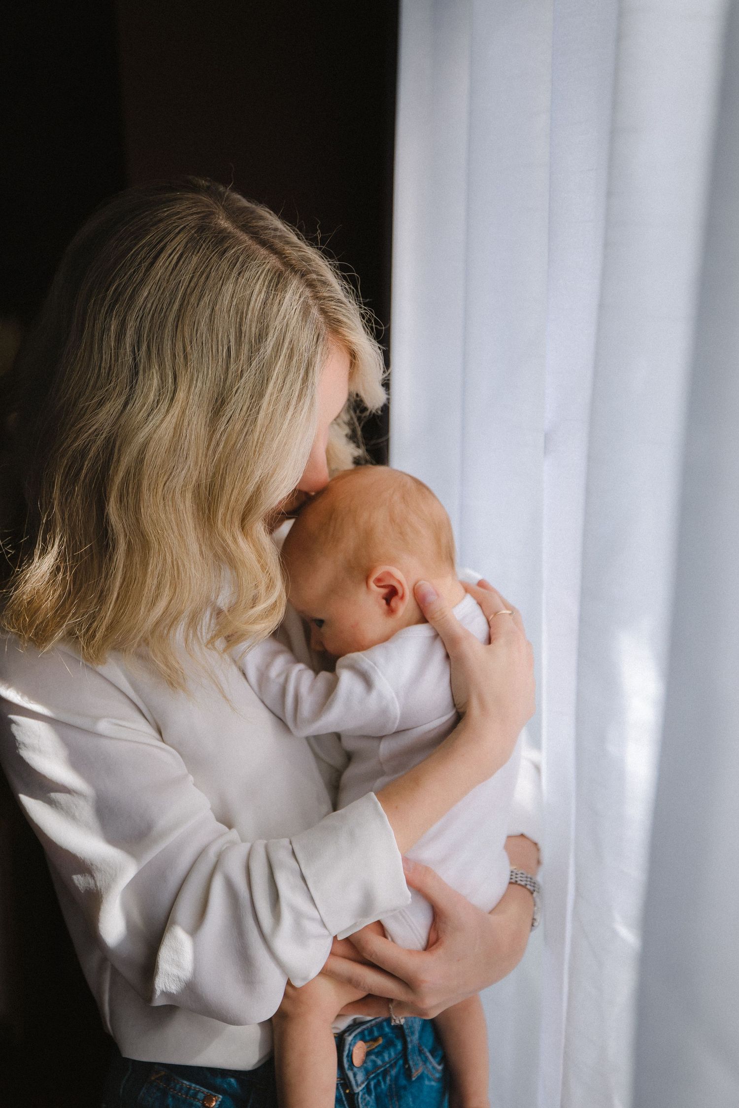 A tender moment between parent and newborn baby by a sunlit window.