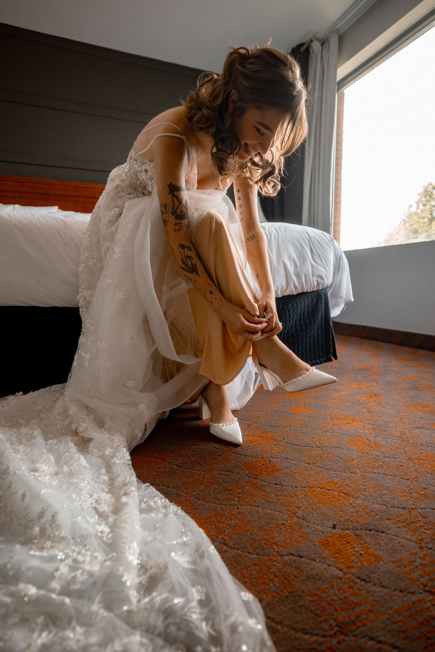 Person in white wedding dress sitting on orange patterned carpet near window.