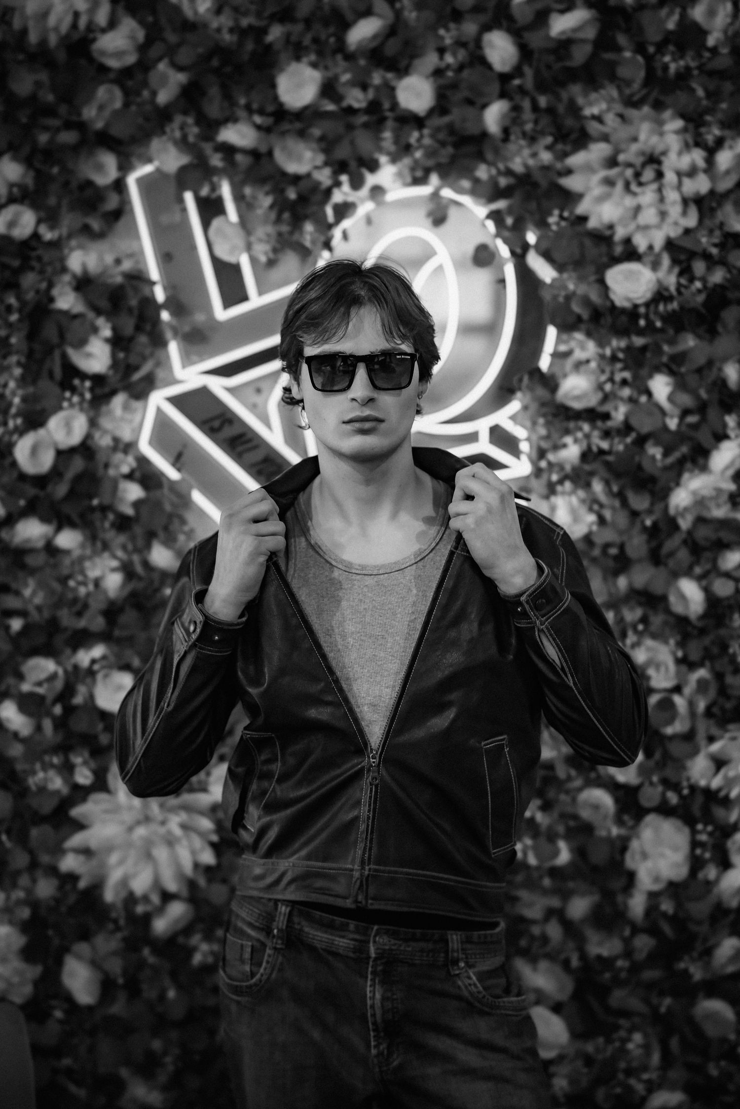 Stylish portrait against floral backdrop with neon lighting and sunglasses.