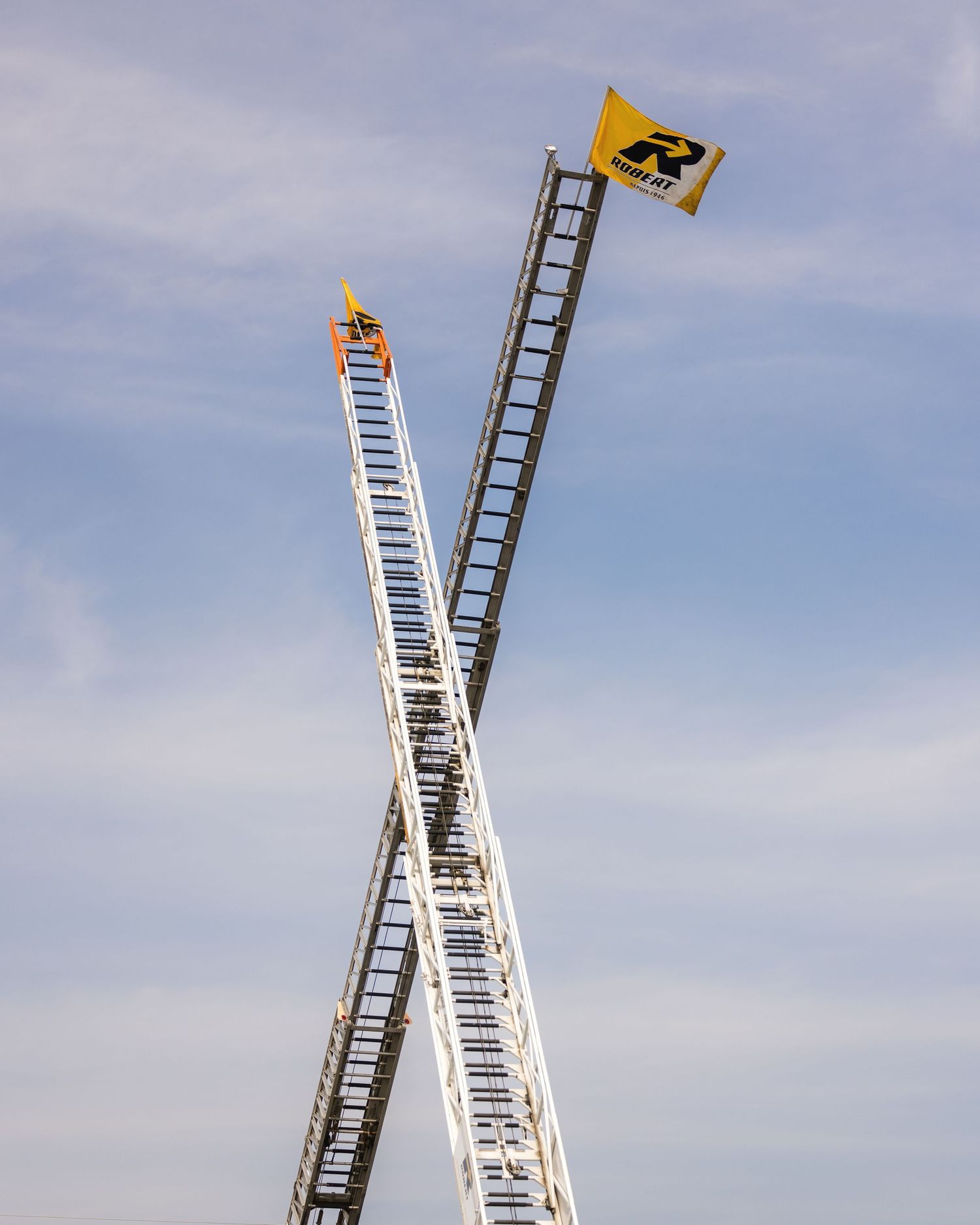 Two tall construction cranes crossing against a blue sky.