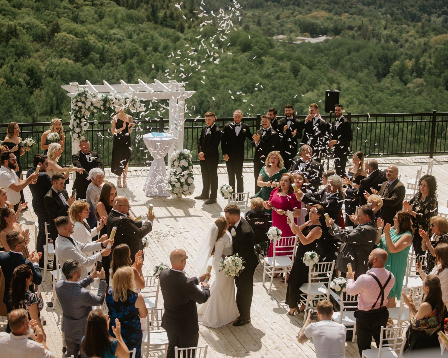 Outdoor wedding ceremony with guests throwing confetti as couple celebrates at mountain venue.