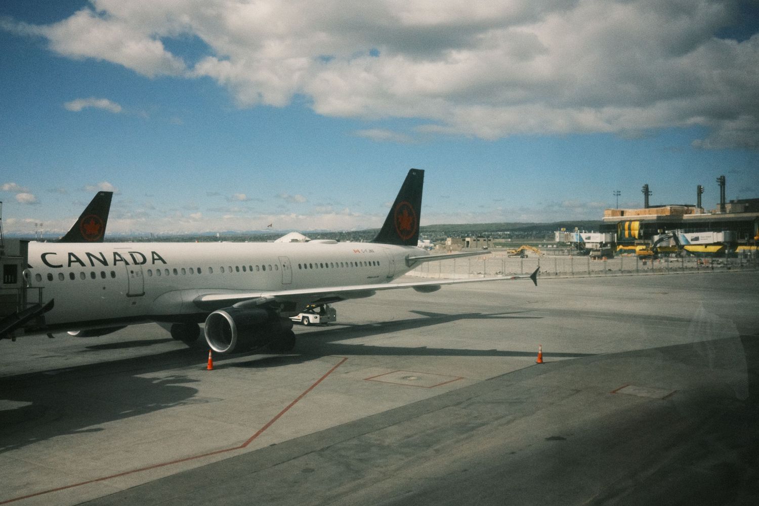 Air Canada passenger jet parked on the tarmac at a busy airport under a partly cloudy sky.