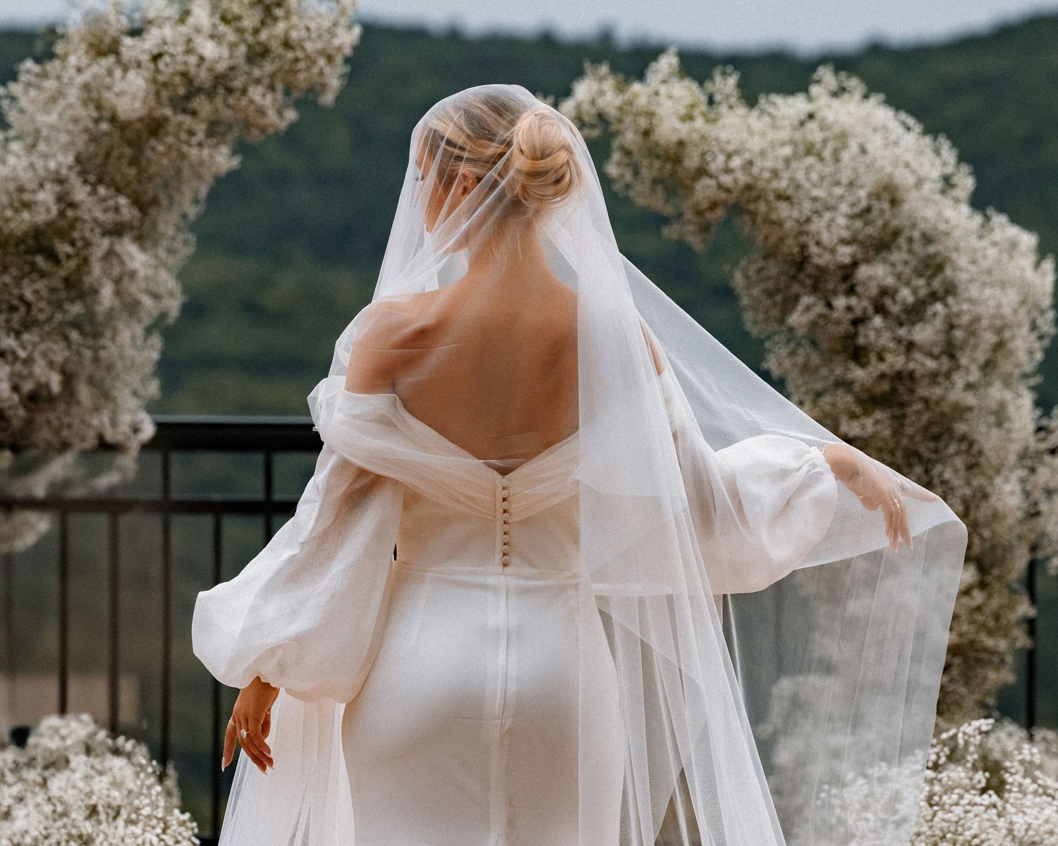Elegant white wedding dress details with flowing veil against natural outdoor backdrop.