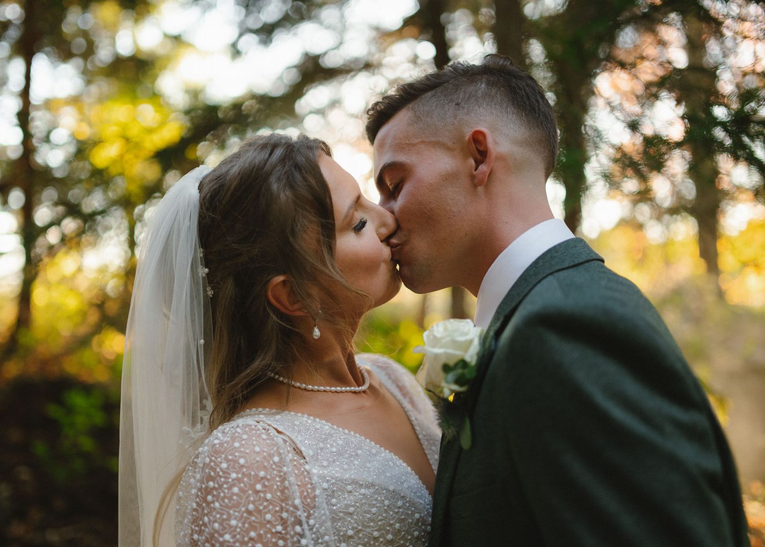 Romantic wedding moment captured in golden sunlight among autumn trees.