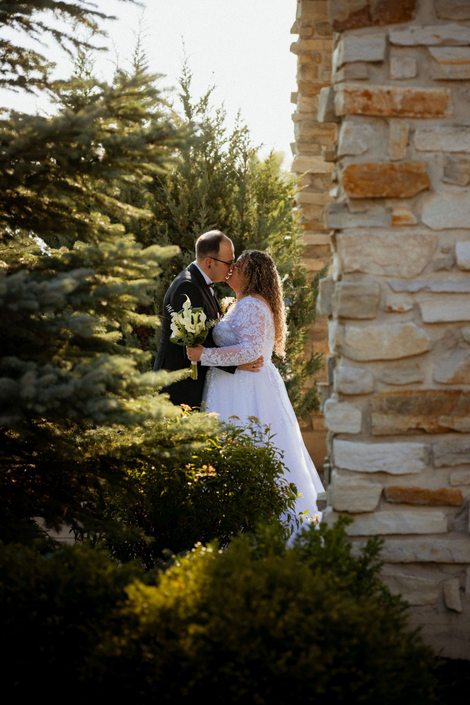 Romantic sunset moment at a stone archway surrounded by evergreen trees.