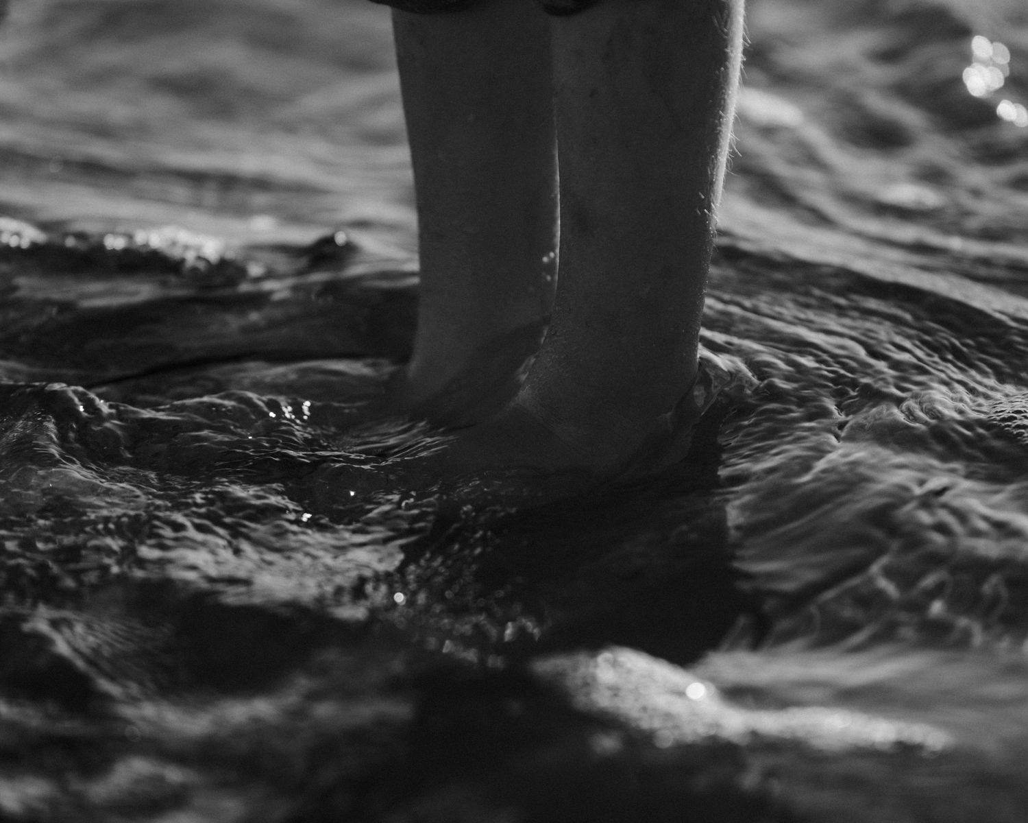 Black and white close-up of feet splashing in rippling water.