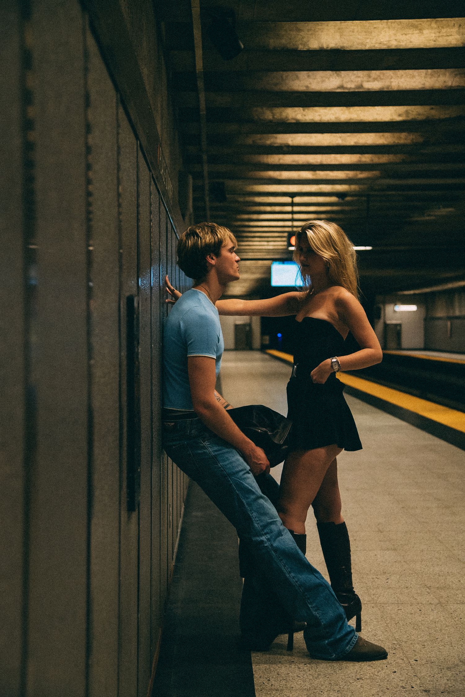 Romantic couple in casual wear posing against wall in subway station.