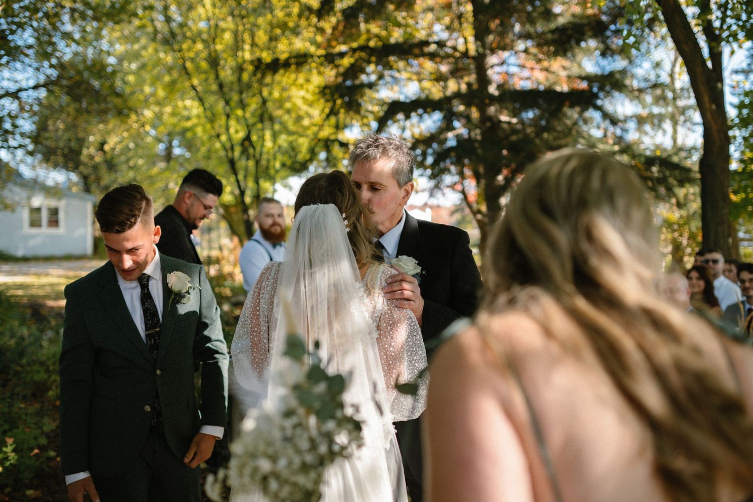 Outdoor wedding ceremony under tall birch trees with golden sunlight filtering through.
