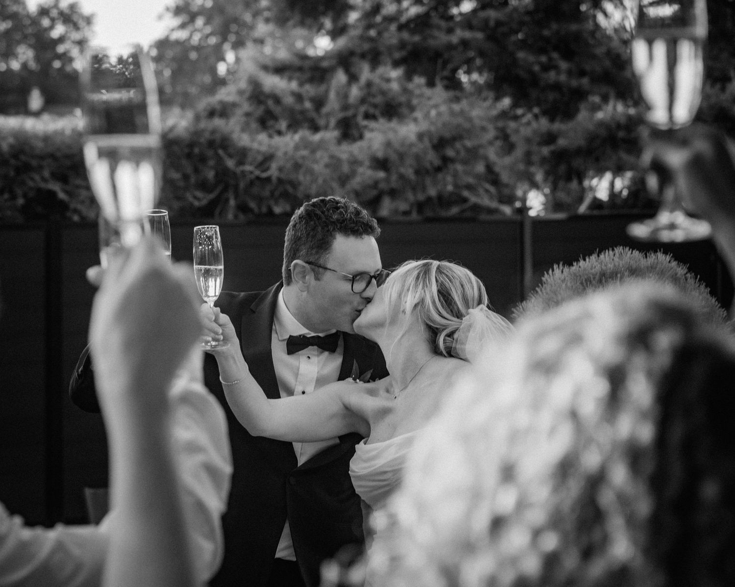 Black and white capture of a wedding toast with champagne glasses raised.