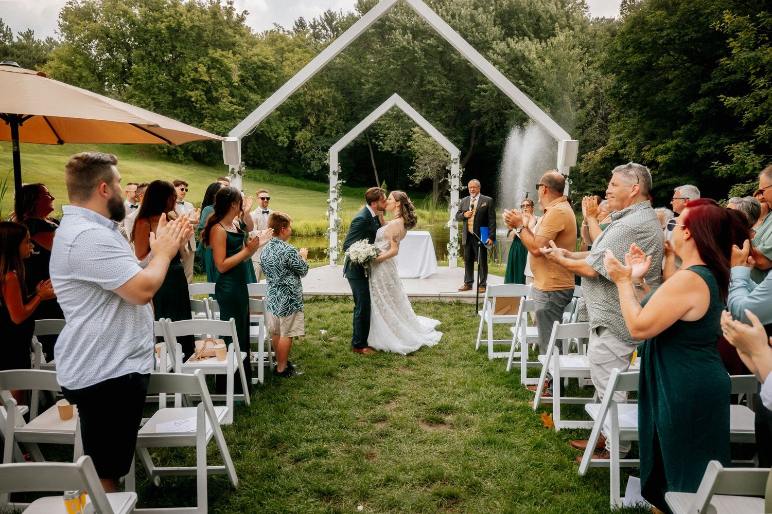 Wedding celebration with guests and white chairs set up on grassy hillside.