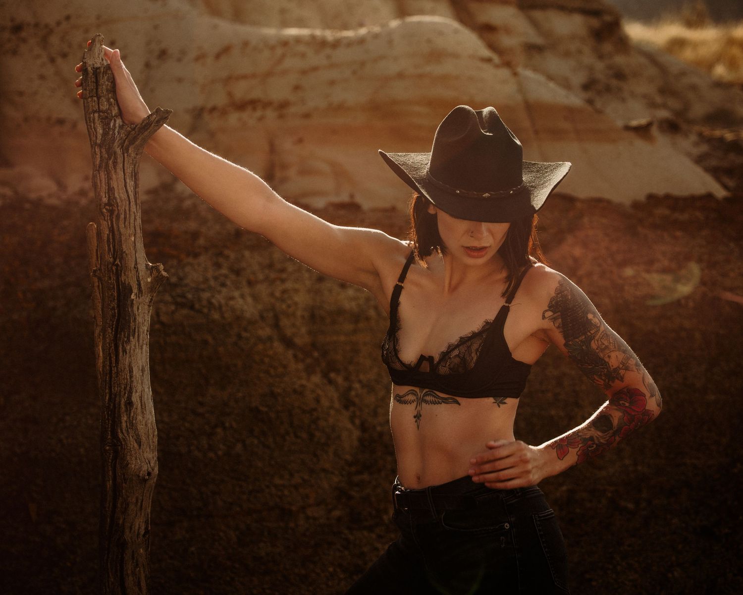 Artistic desert photoshoot with cowboy hat and dramatic lighting.