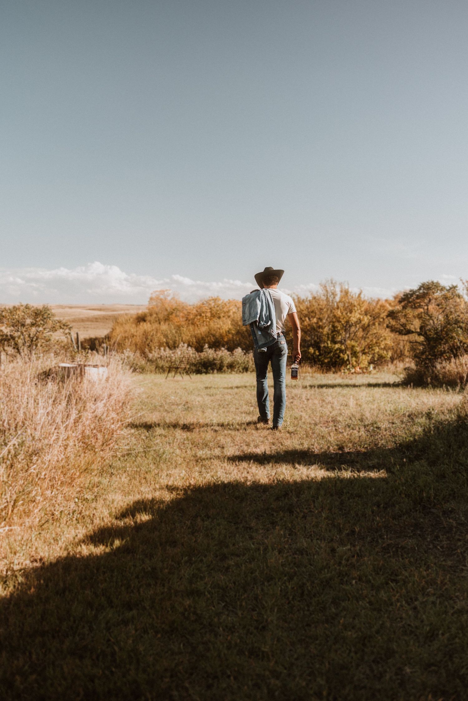 Person in cowboy hat walking through golden autumn field at sunset.