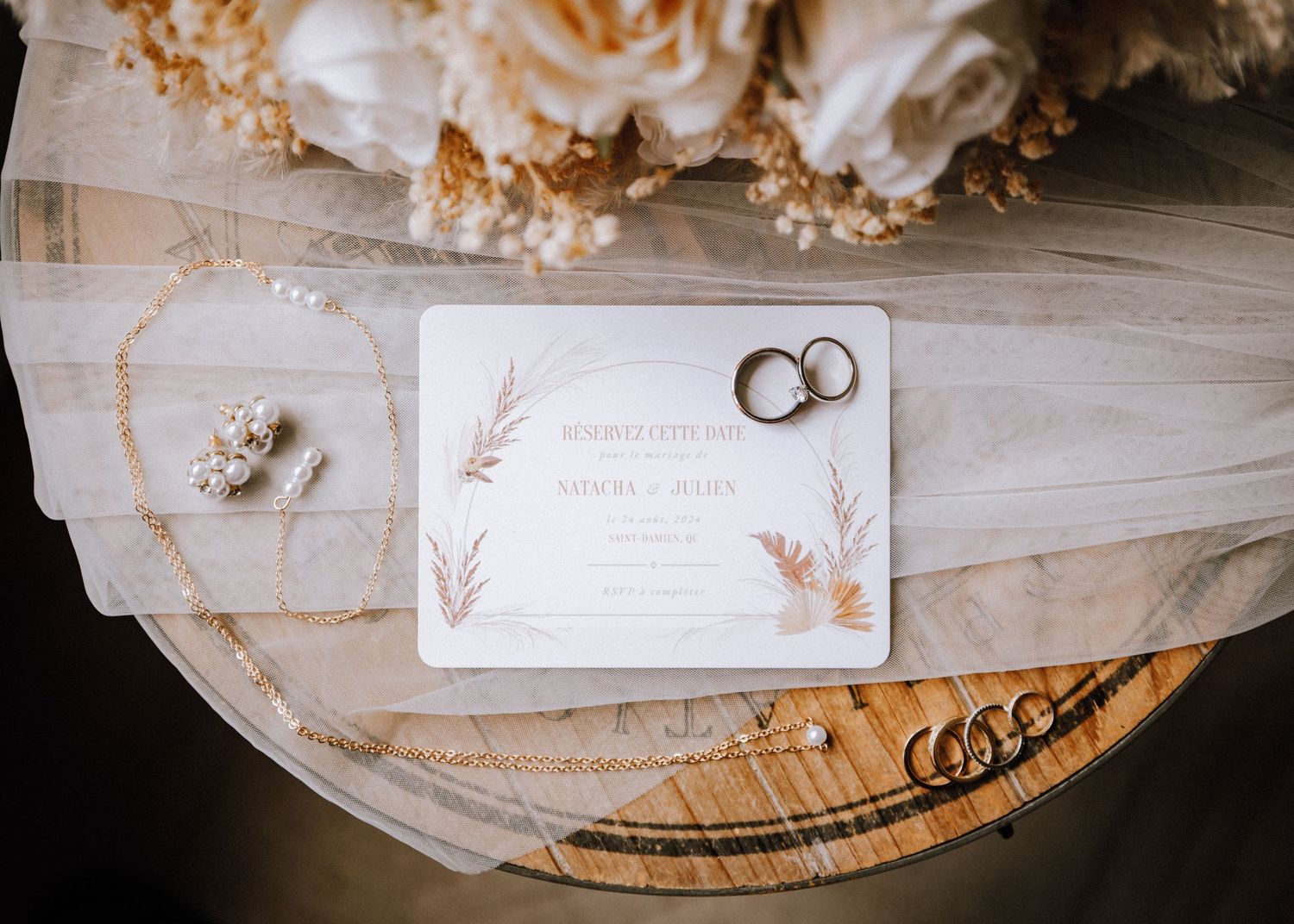 Wedding rings and invitation details photographed on white fabric with delicate lace accents.