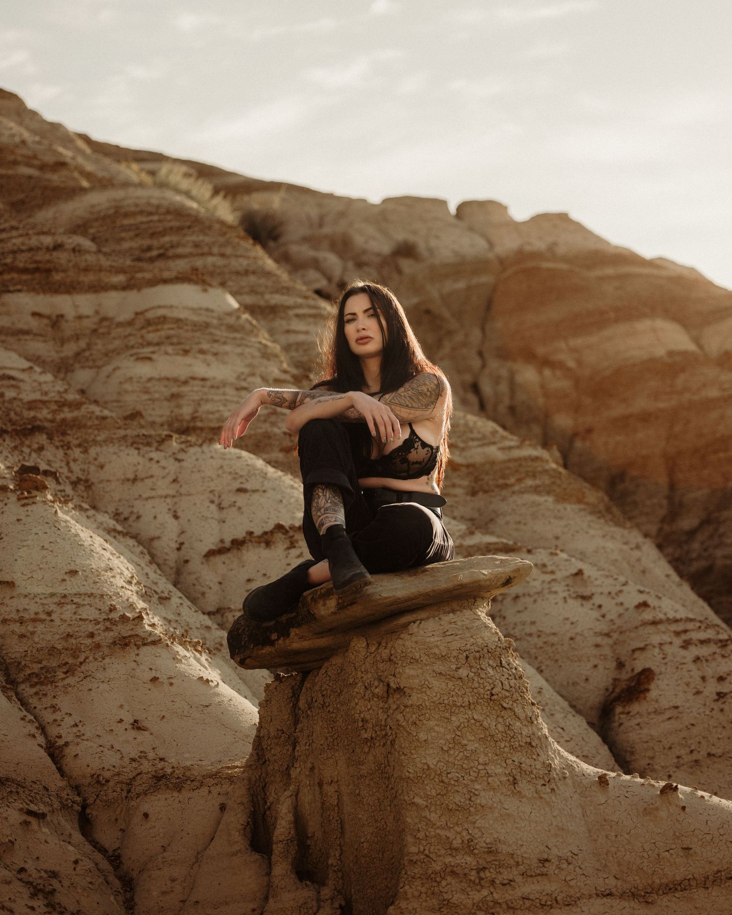 Figure in dark clothing sits on rocky desert terrain during golden hour.