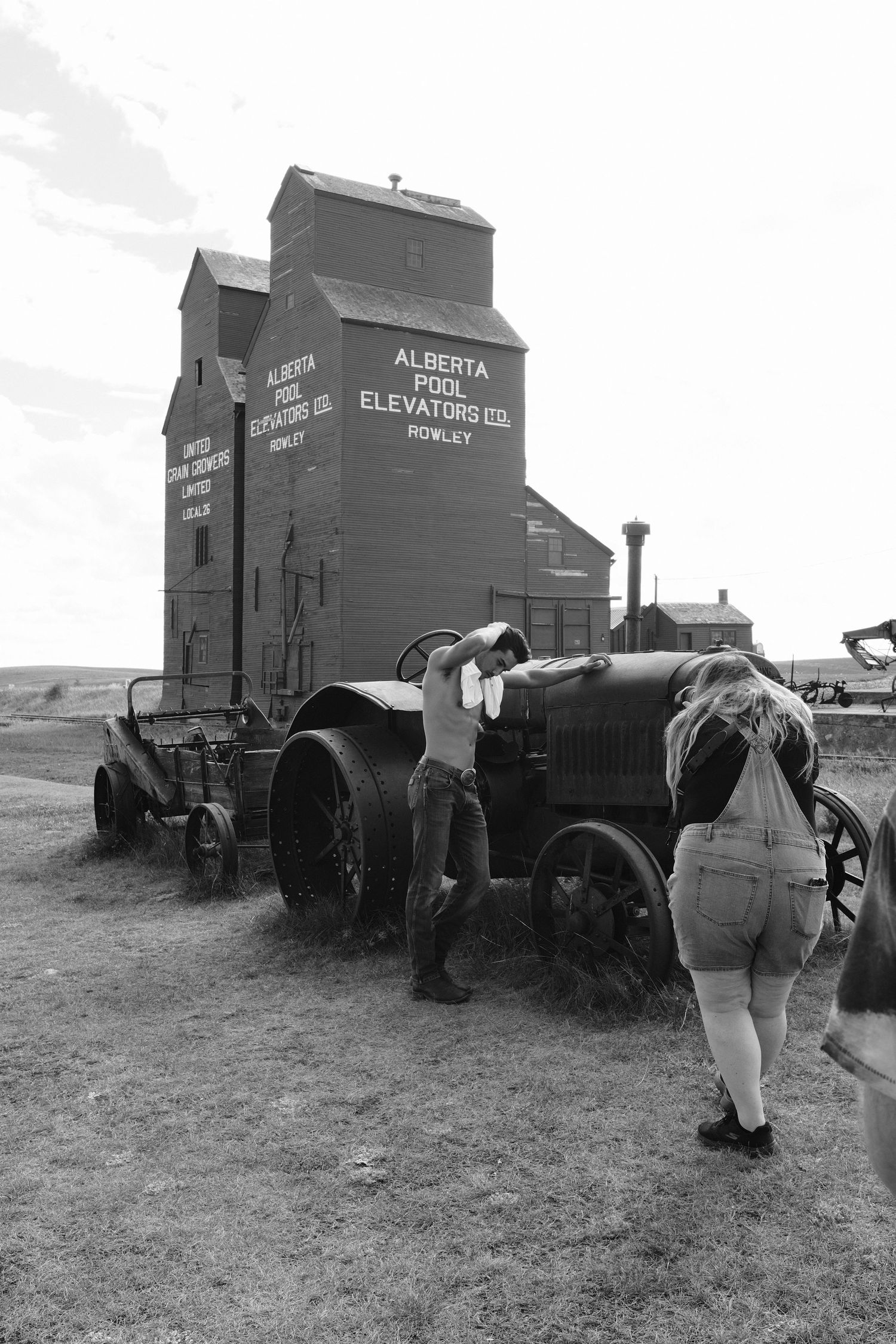 Black and white photo of people examining vintage farm equipment near Alberta Pool Elevators grain elevator in Rowley.