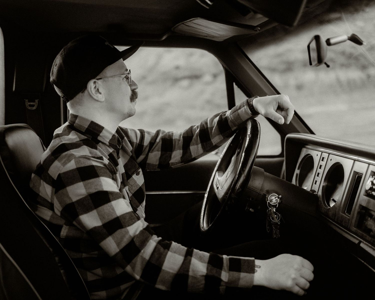 Person in plaid flannel shirt driving a vehicle in black and white photography.