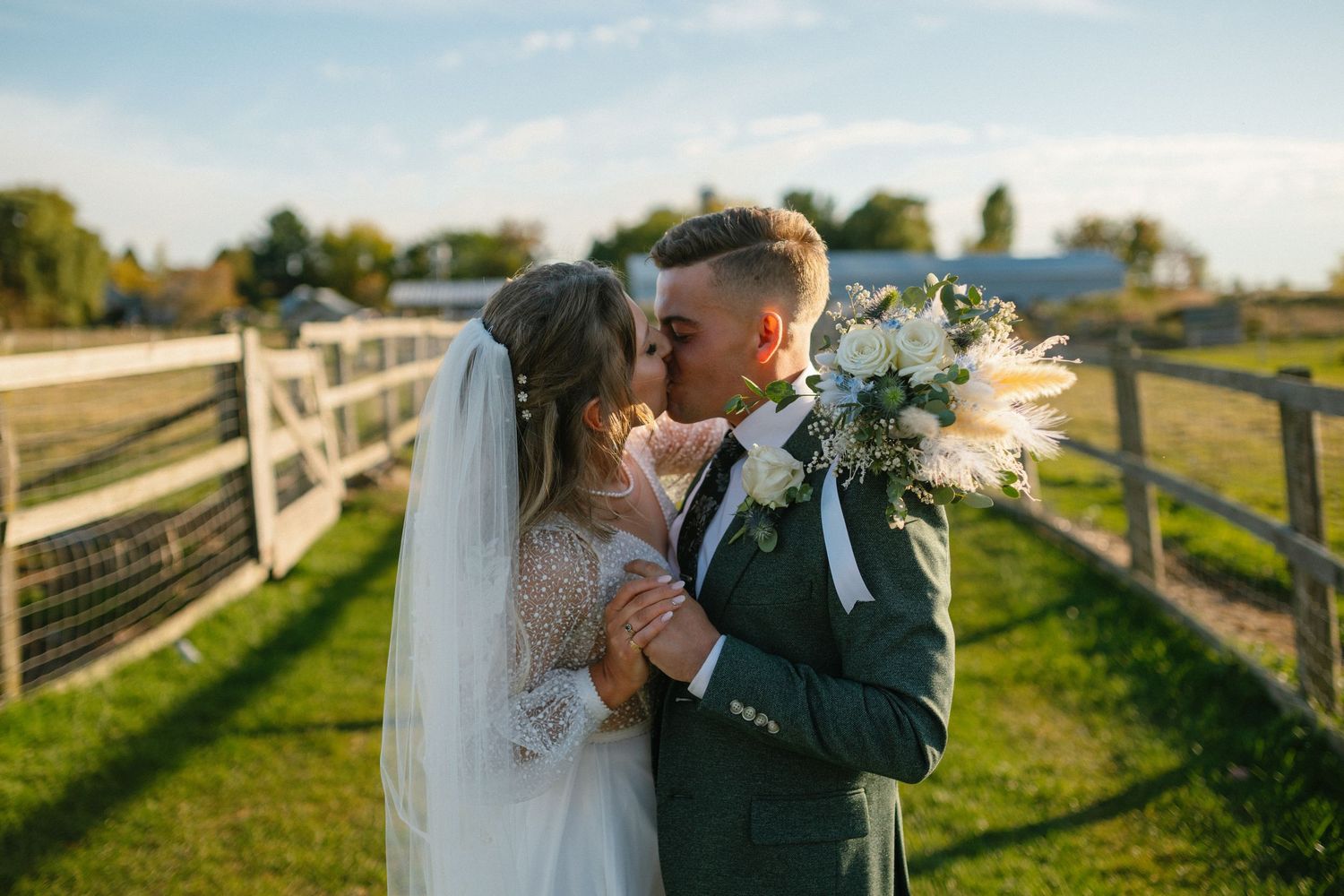 Couple shares intimate moment by rustic fence during golden hour.