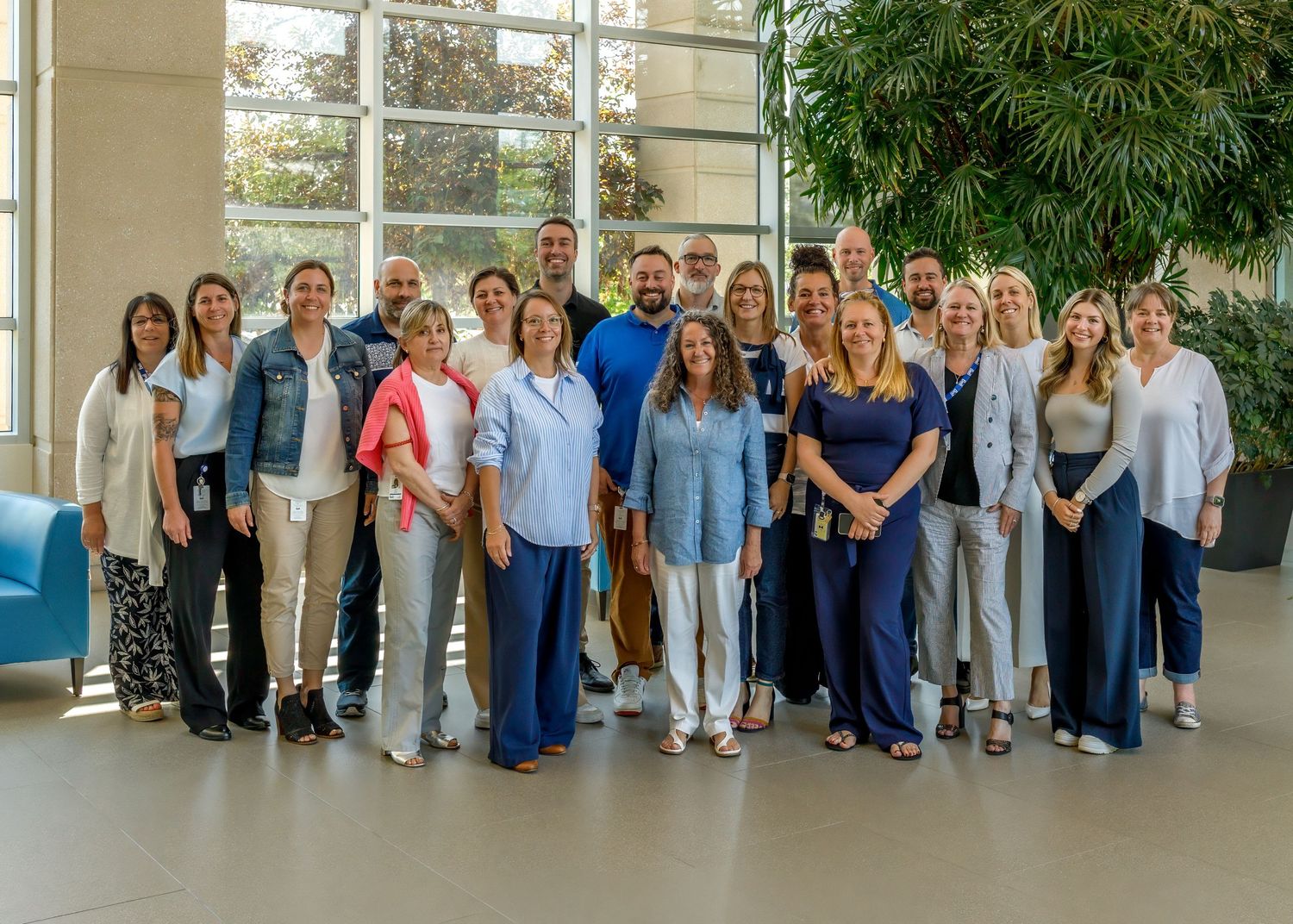 Large group photo of staff members standing together in a bright indoor space with plants.