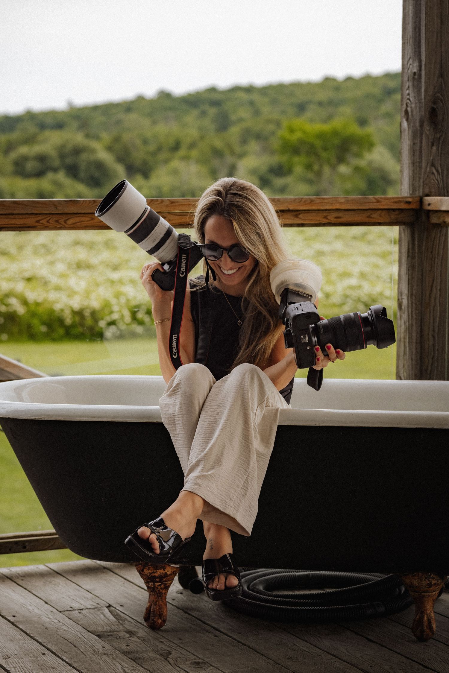 Professional photographer with cameras working in vintage clawfoot bathtub on rustic porch.