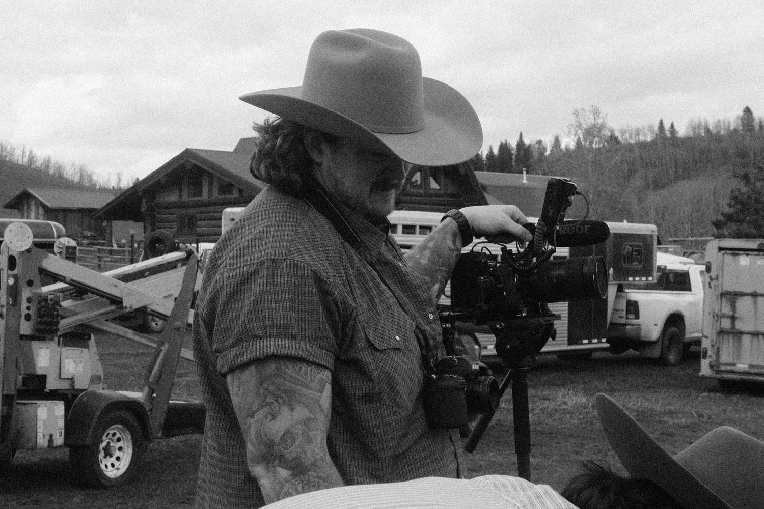 Cinematographer wearing cowboy hat operating professional camera on rural film set in black and white photo.