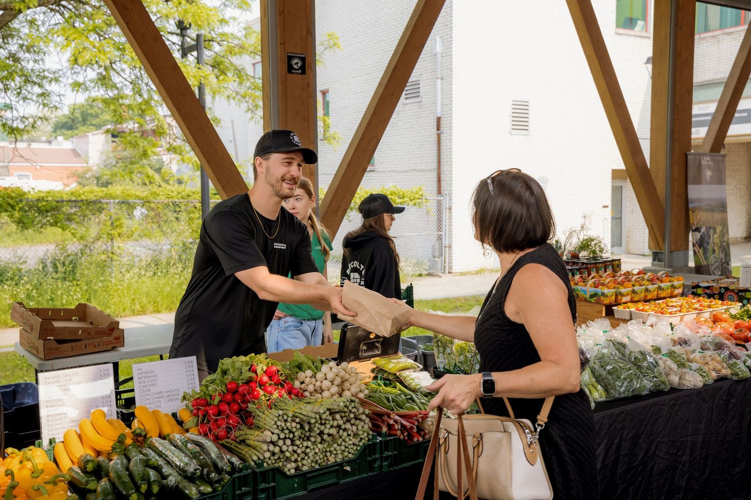 Farmer selling fresh produce to customer at outdoor market stand.