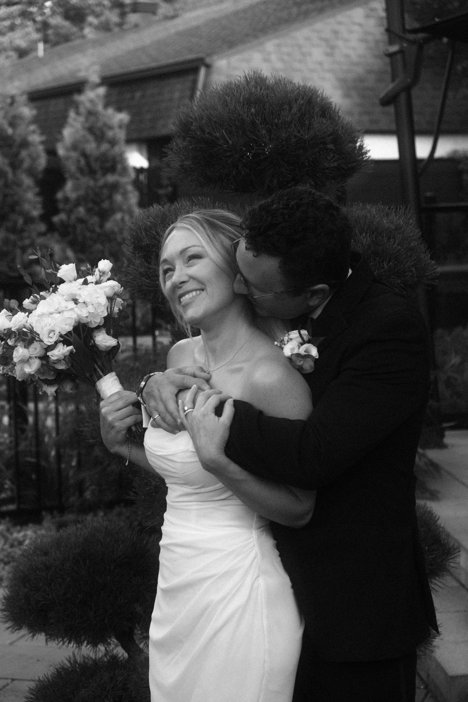 Black and white portrait of newlyweds embracing with bride holding bouquet.
