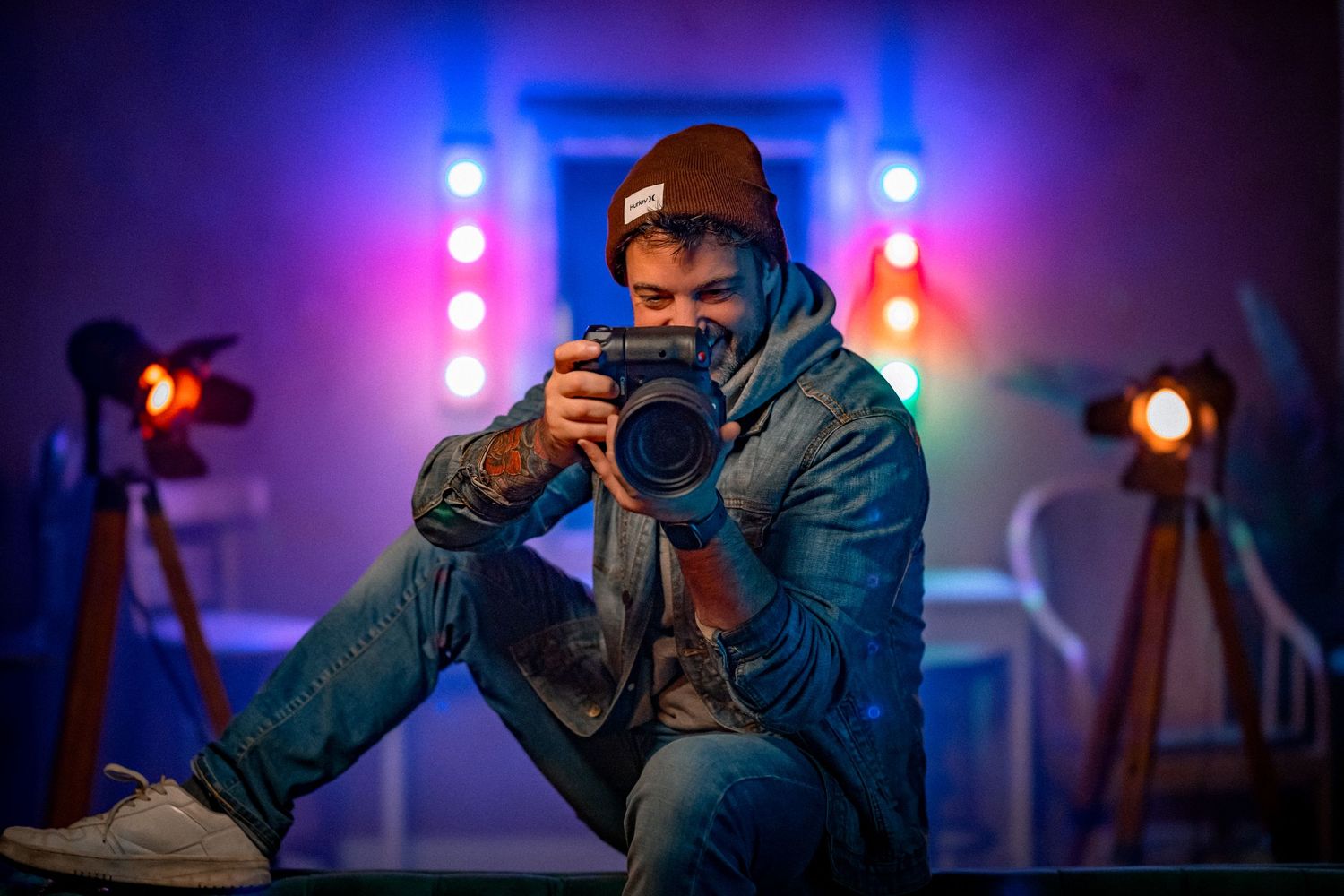 Silhouette of photographer working with camera equipment in dark studio with blue and pink lighting.