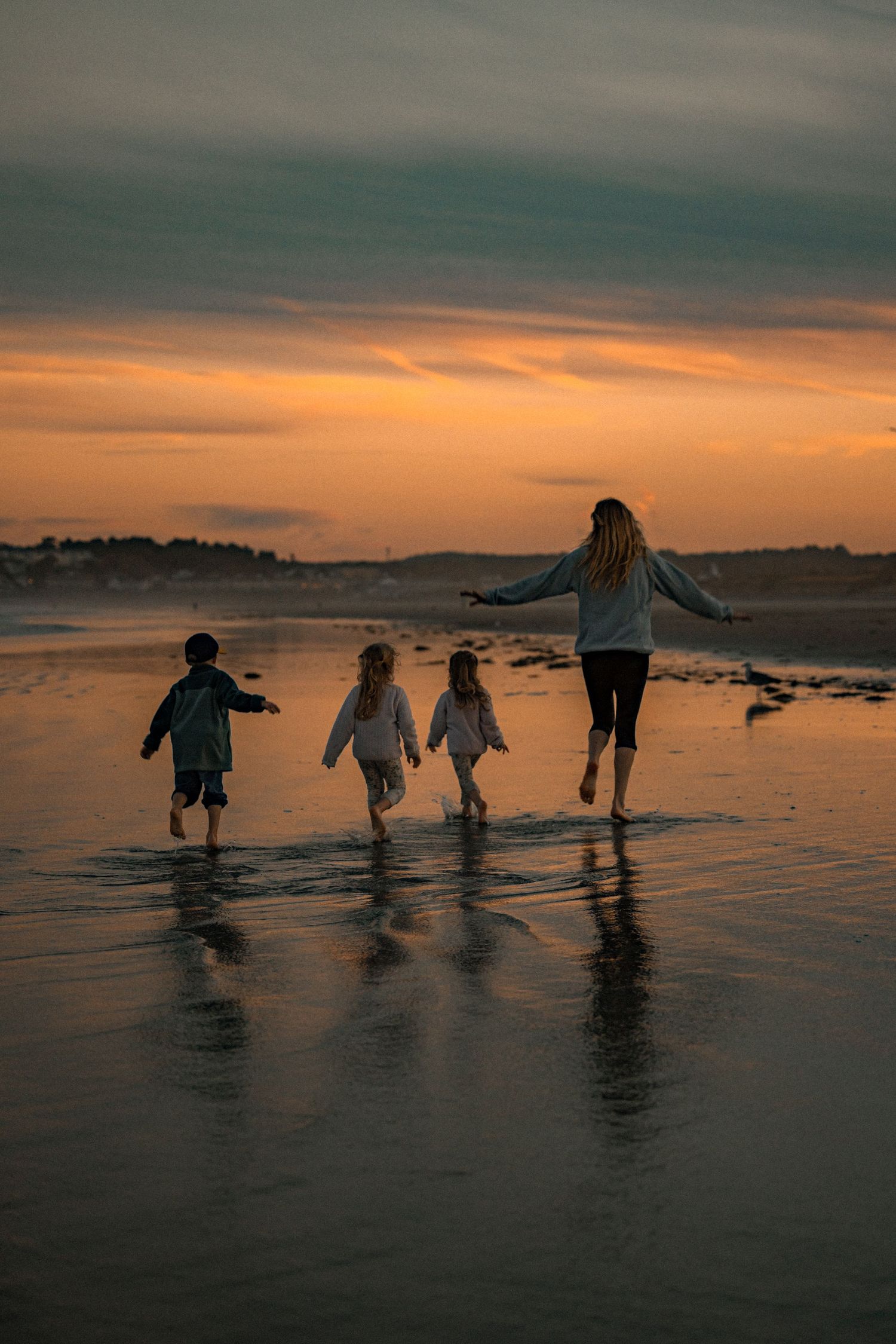 Silhouettes of people playing in shallow water against a dramatic orange sunset sky.