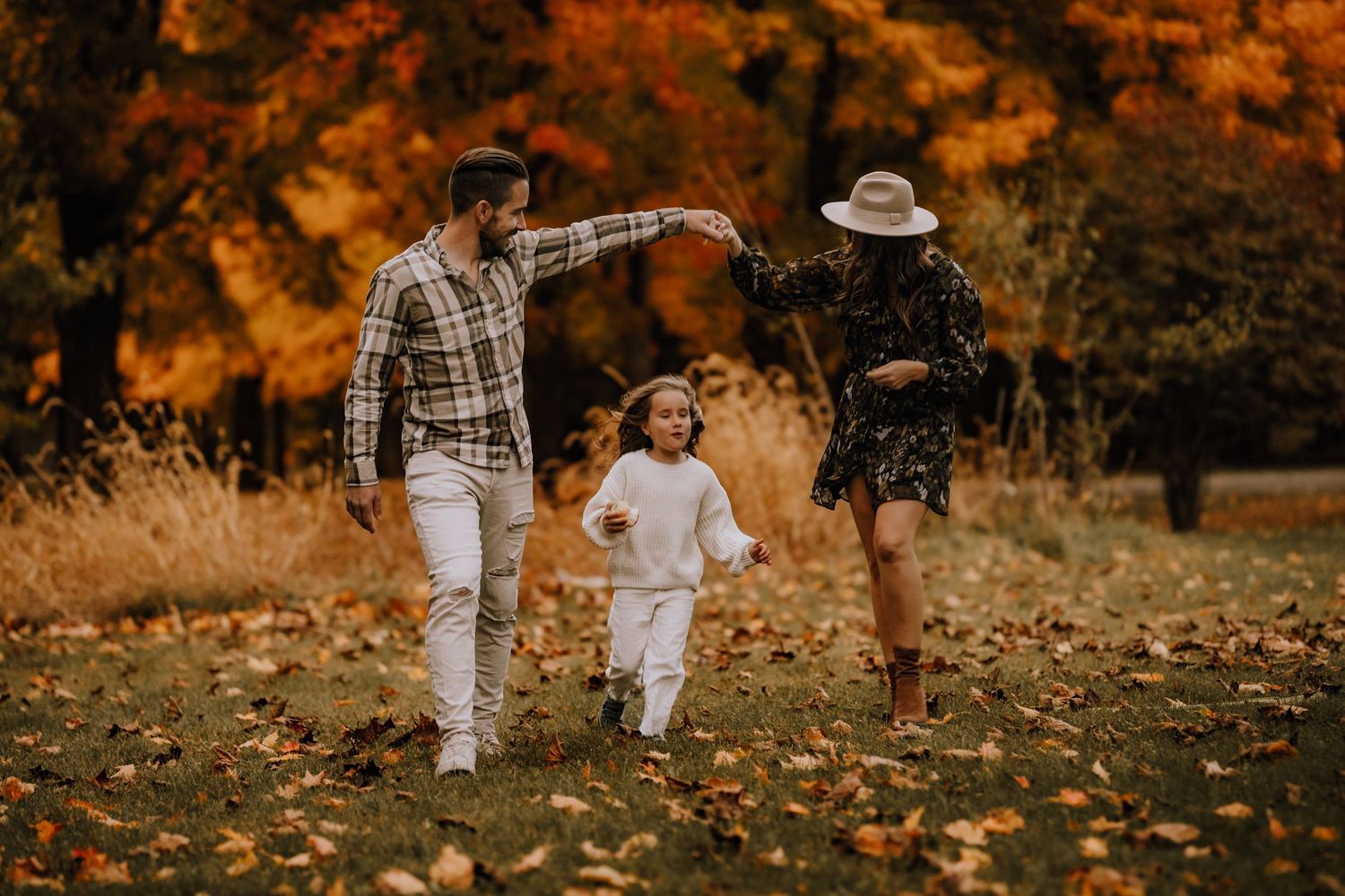 People strolling through fallen leaves in a park during peak autumn colors.