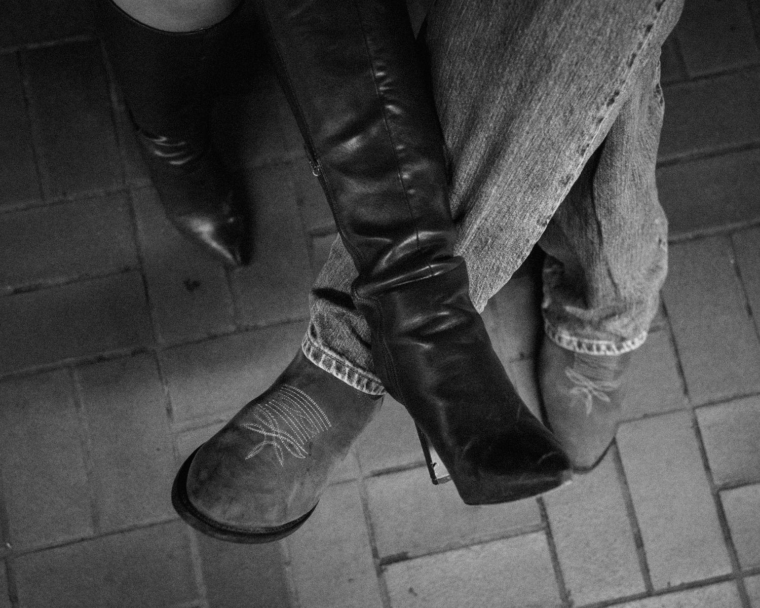 Close-up of two pairs of boots touching on tiled floor.