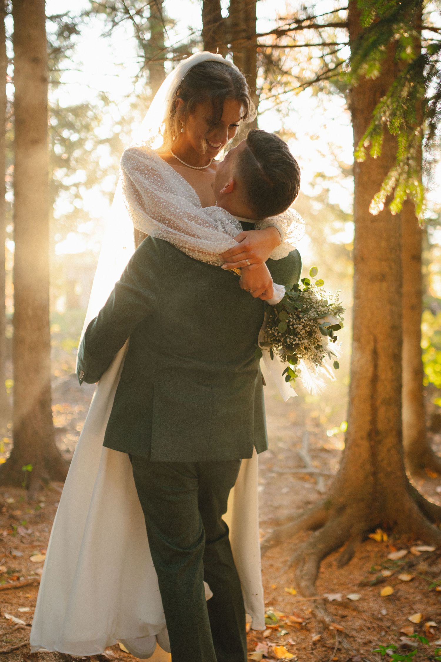 Romantic embrace between newlyweds in a sunlit forest setting.