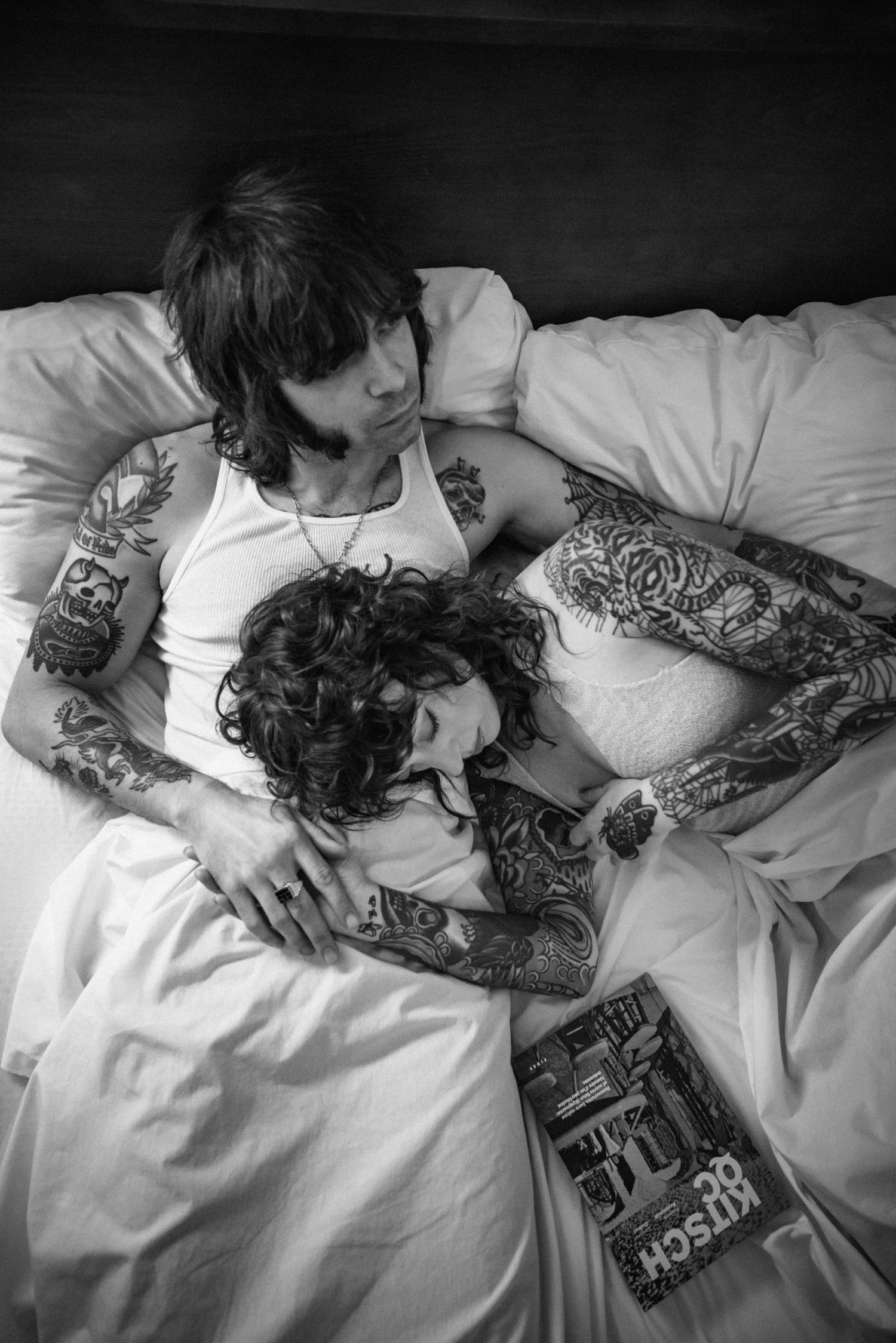 Black and white image of tattooed couple sharing intimate moment in bed.
