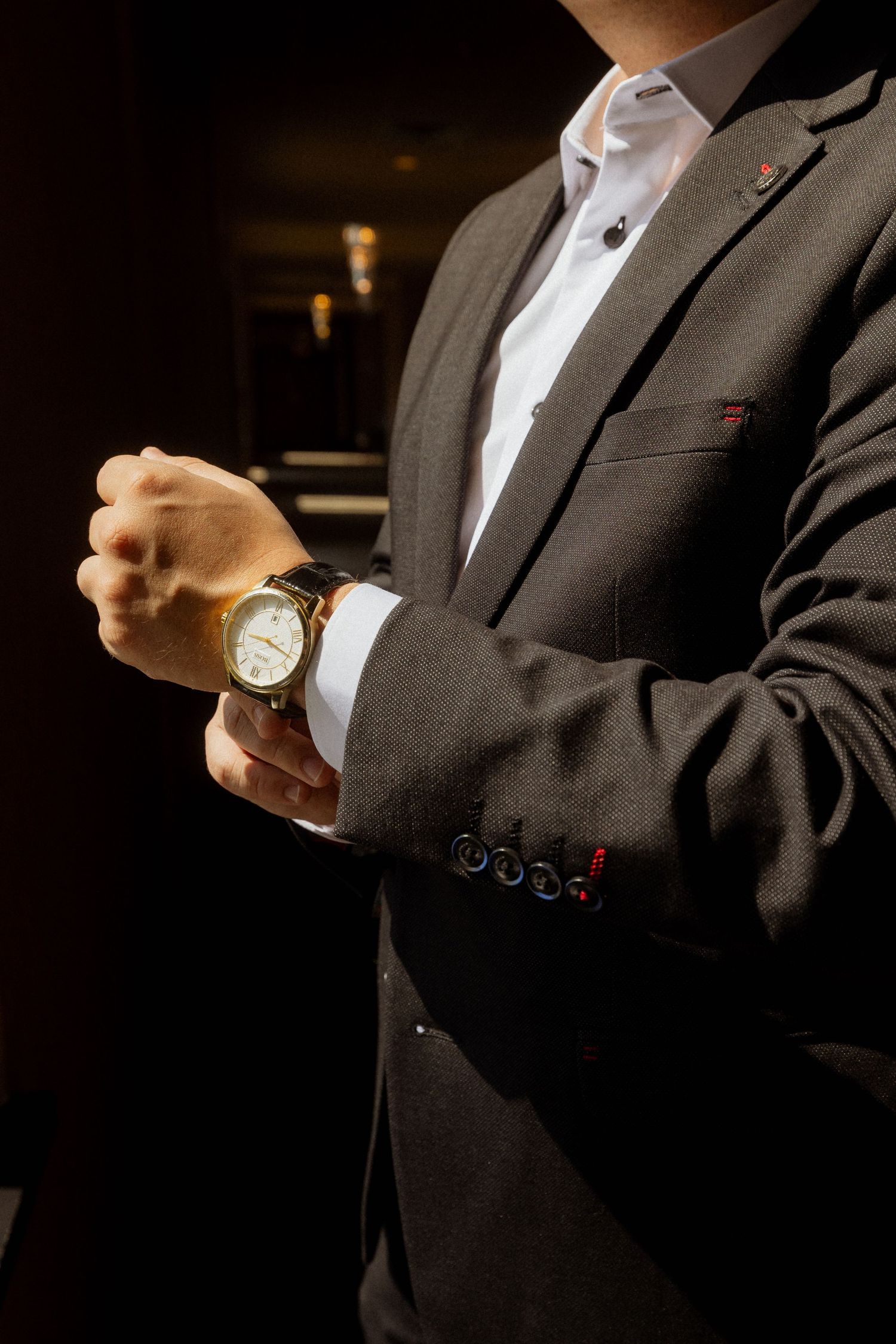 Close-up shots of groom adjusting watch and suit cuffs in dramatic lighting.