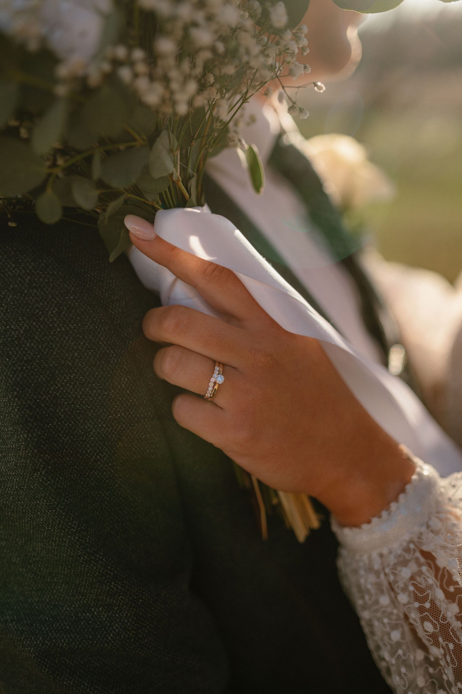 Close-up of hands wearing a wedding ring holding delicate white flowers against a dark fabric background.