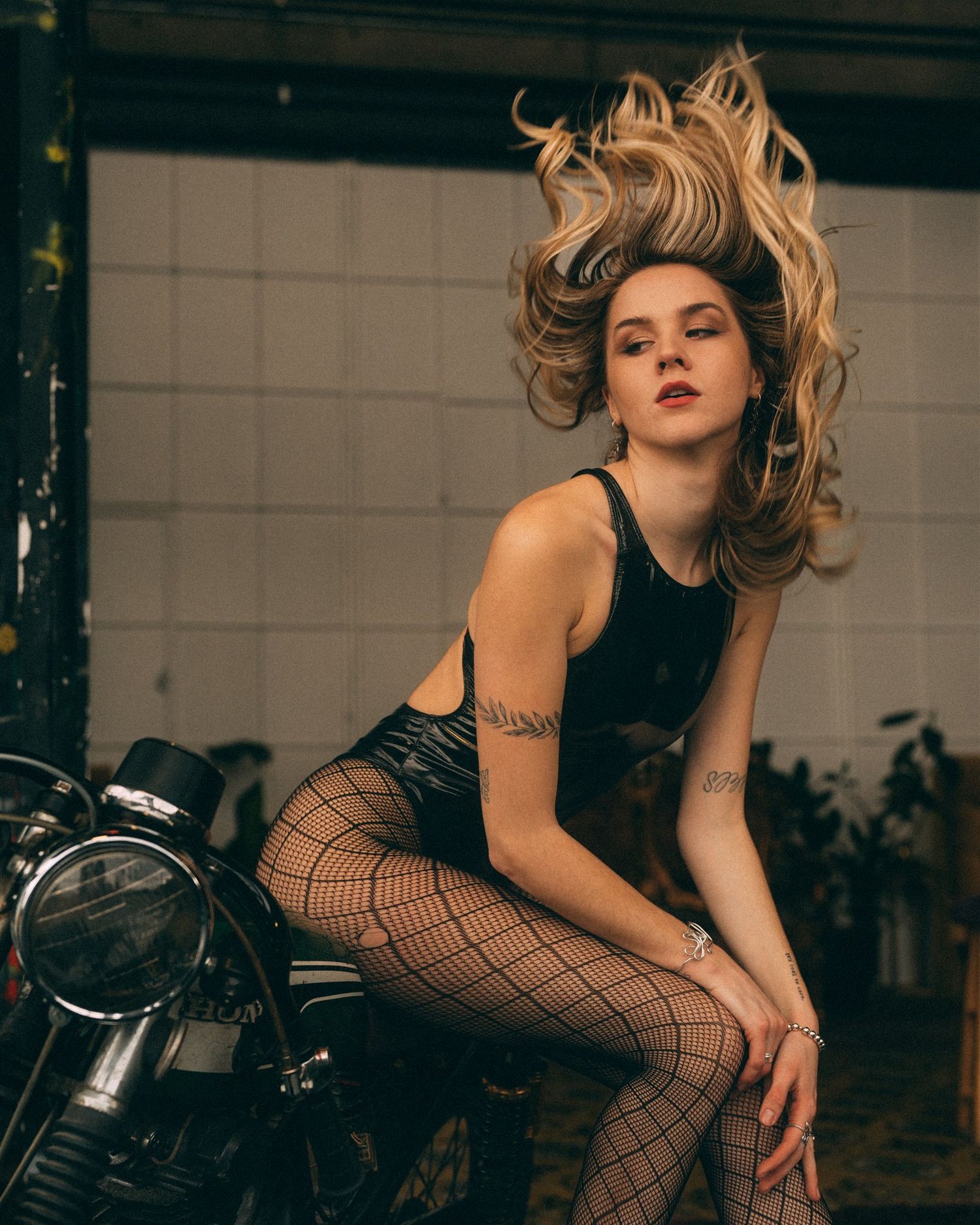Woman in fishnet stockings poses dramatically on vintage motorcycle.