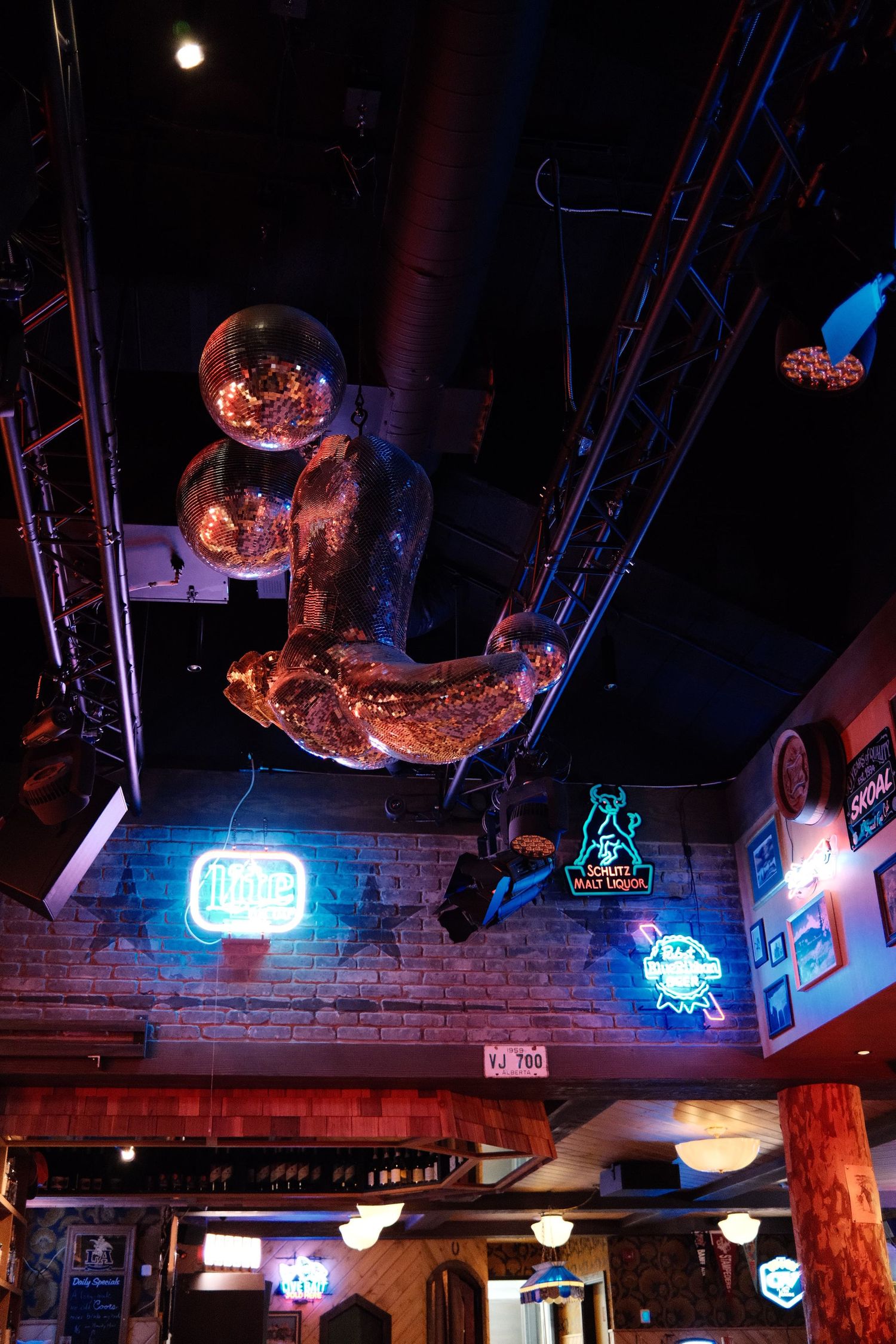Bar interior with neon signs, brick walls, and a metallic astronaut sculpture hanging from a dark industrial ceiling.