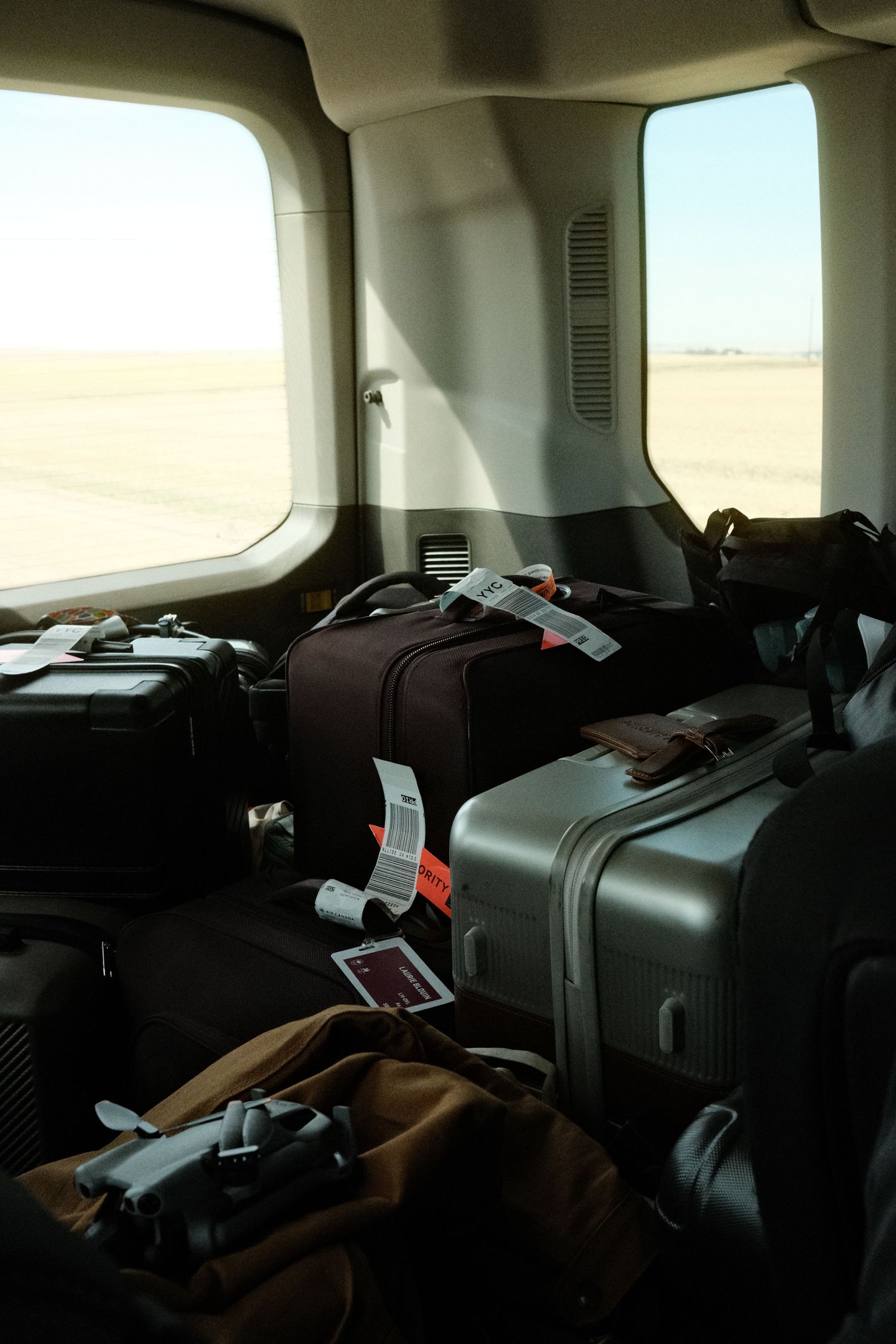 Luggage and bags with airline tags stacked inside a small aircraft cabin with desert runway visible through windows.